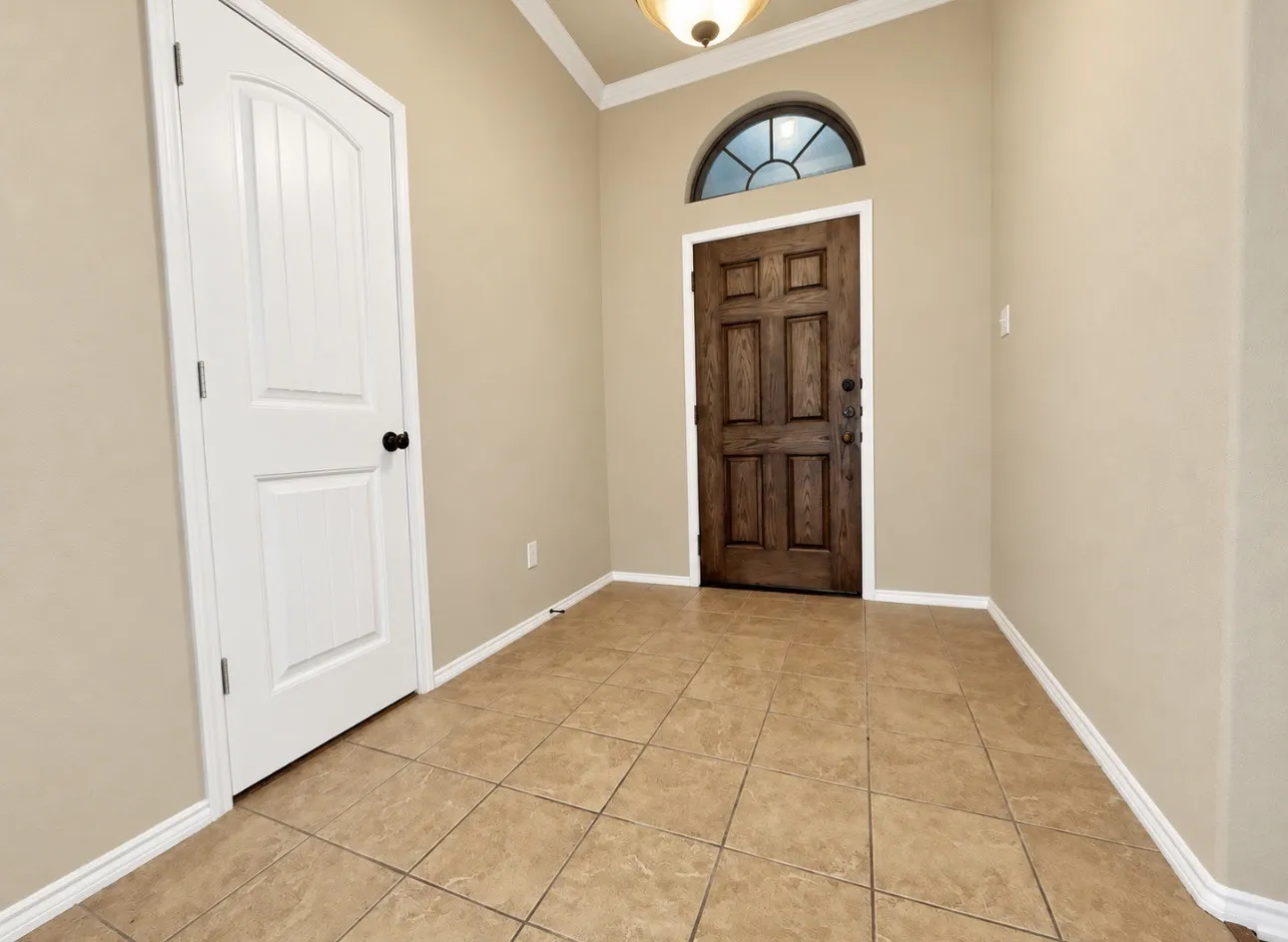 Arch-top entry door with transom window, tile flooring, white baseboards, and crown molding