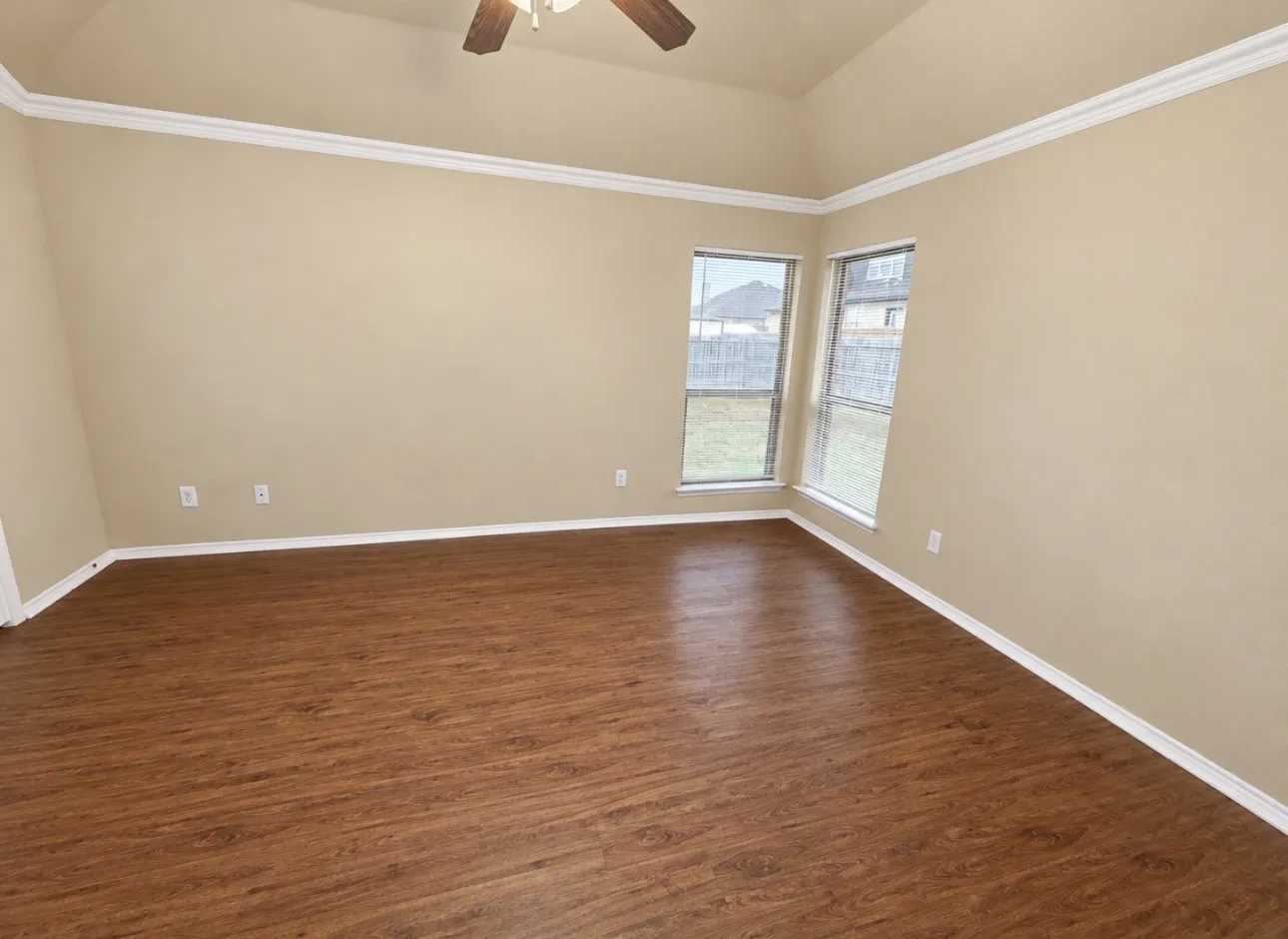 Vaulted ceiling with a ceiling fan, crown molding, wood-finish flooring, and multiple windows