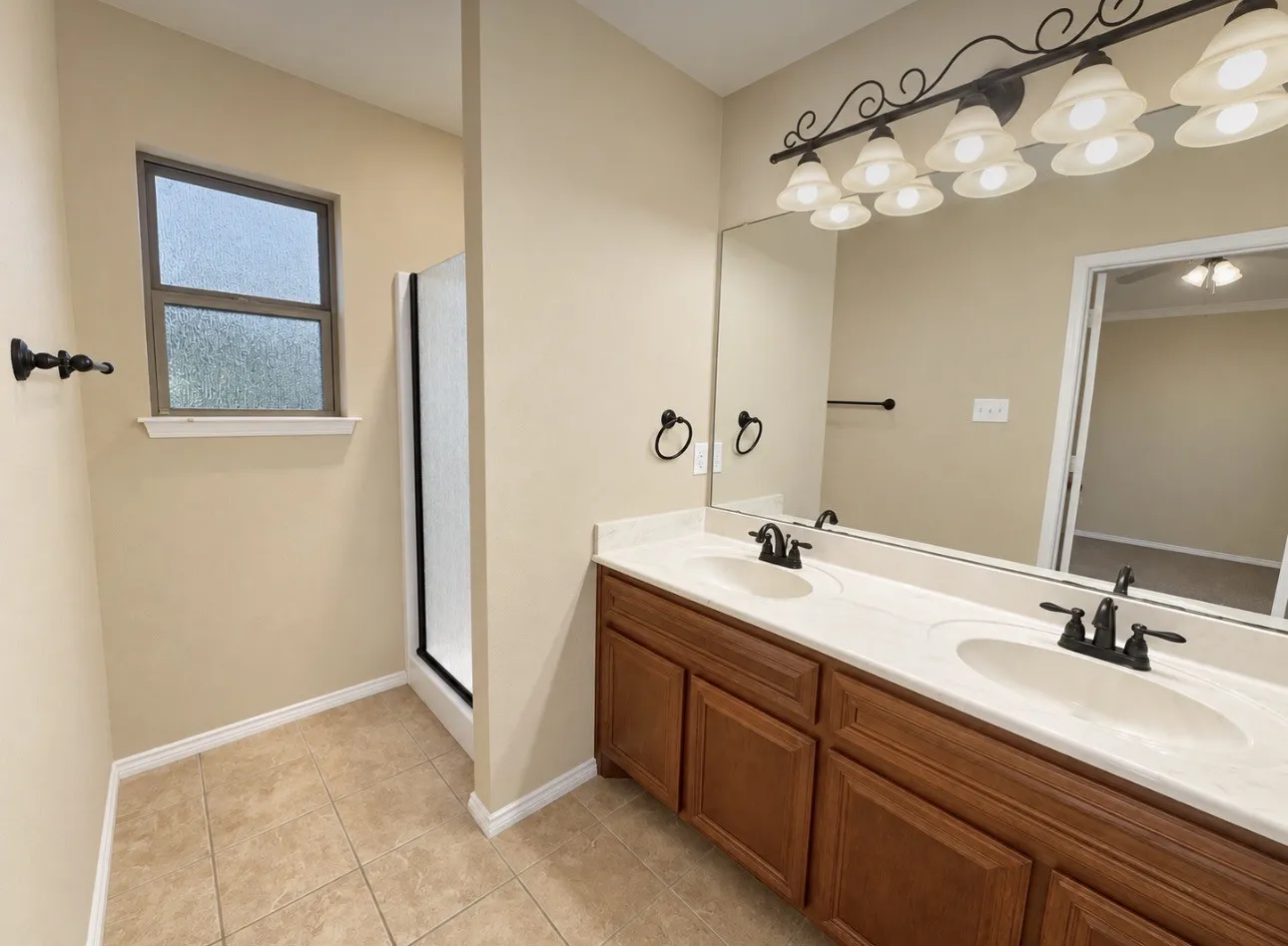 Double vanity with integrated sinks, wood-finish cabinetry, a large mirror, and a multi-bulb light fixture