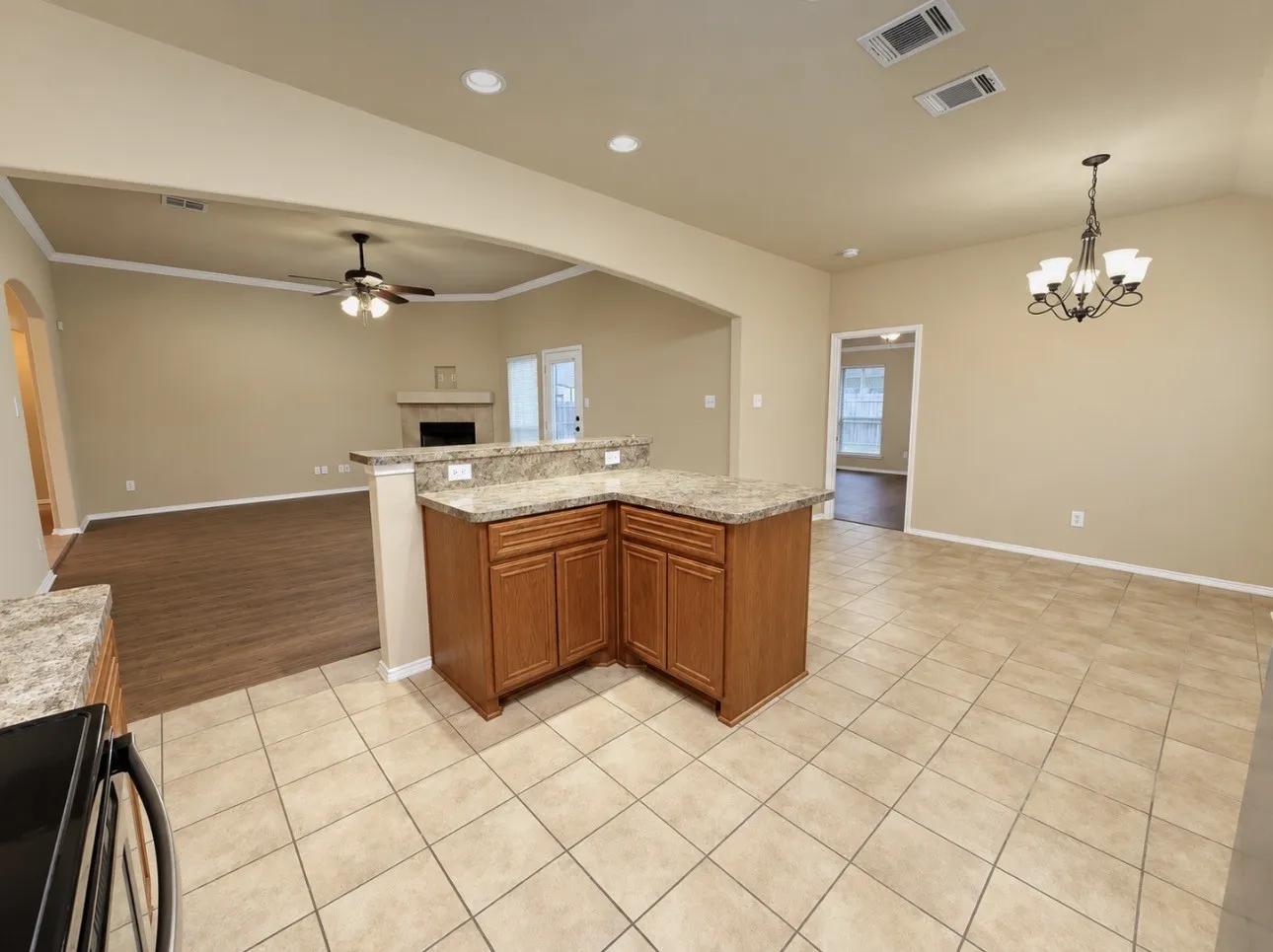 Kitchen featuring L-shaped island with stone-finish countertop, wood-finish cabinetry, and ceramic tile flooring