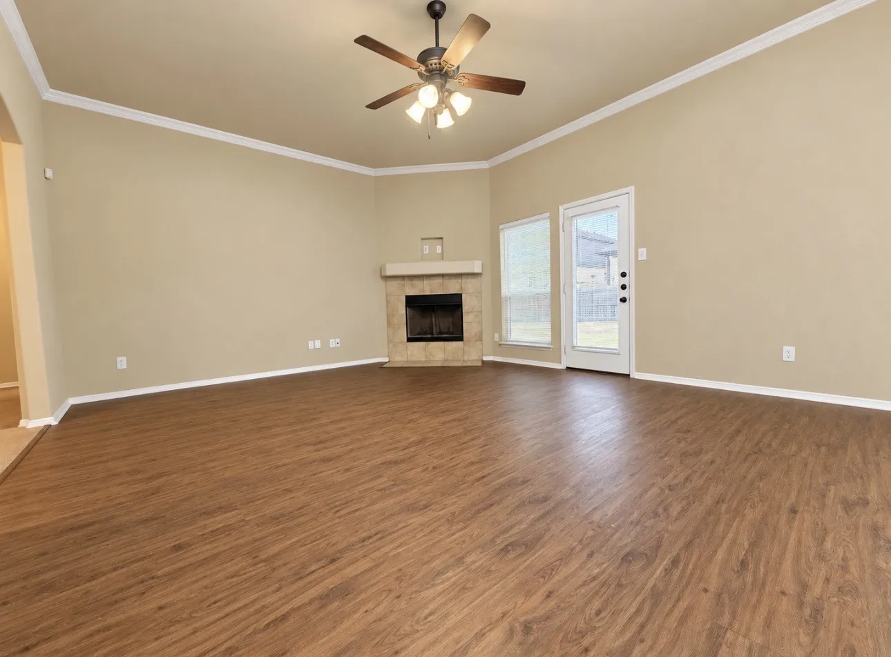 Spacious room featuring wood-finish flooring, a tile-surround fireplace, a ceiling fan with integrated lighting, and crown molding