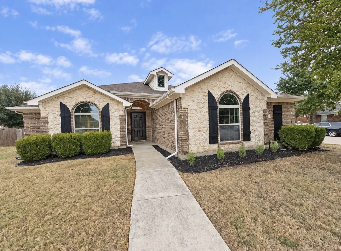 Brick and stone exterior featuring arched windows with dark shutters, a dark paneled entry door, and a dormer window