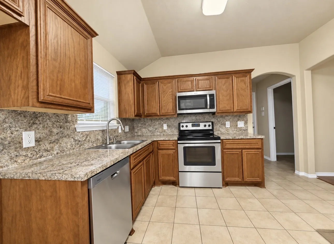 Kitchen featuring wood cabinetry, stainless steel appliances, dual basin sink, and tile flooring