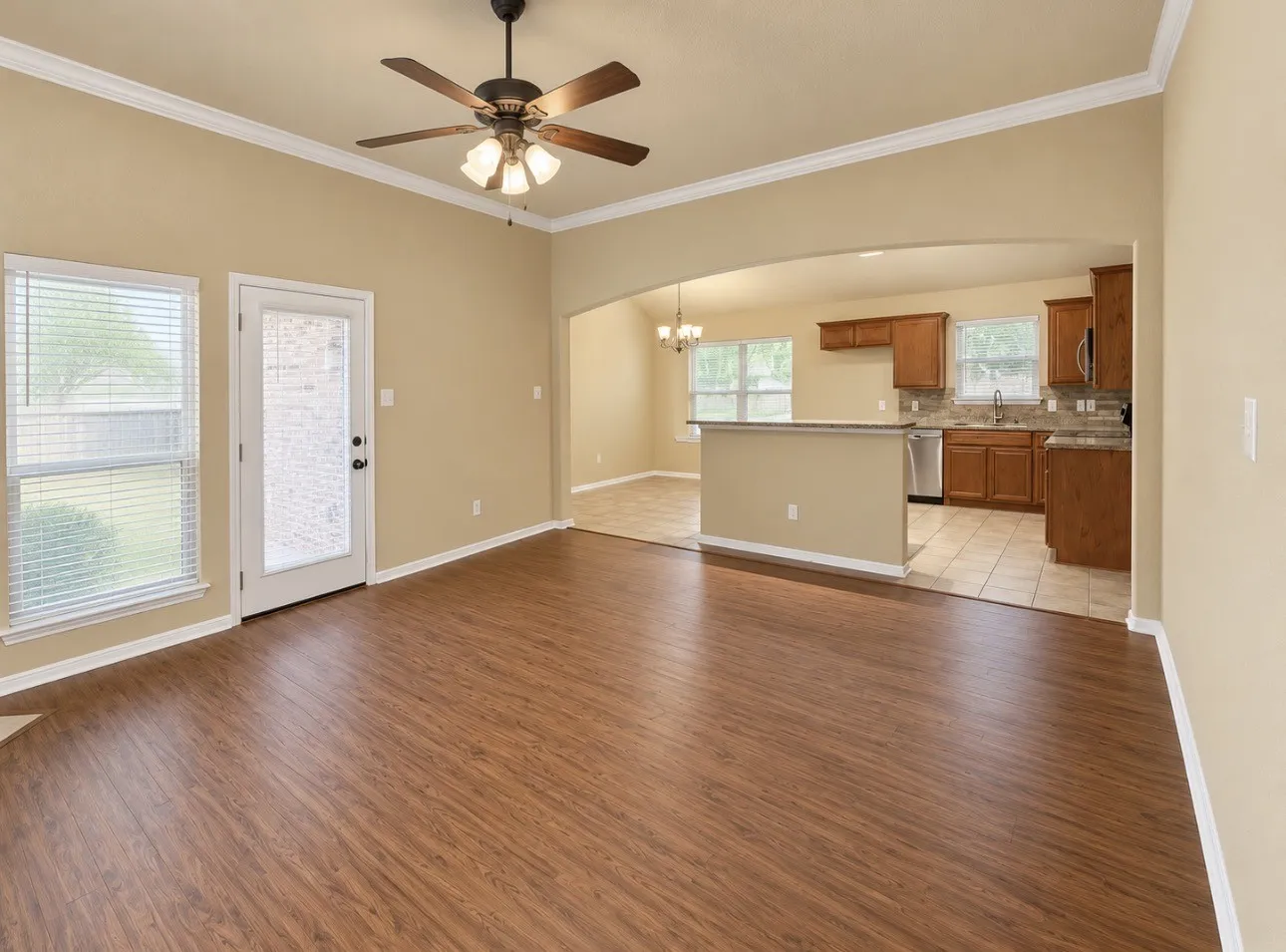 Expansive room featuring wood-finish flooring, a ceiling fan, and crown molding