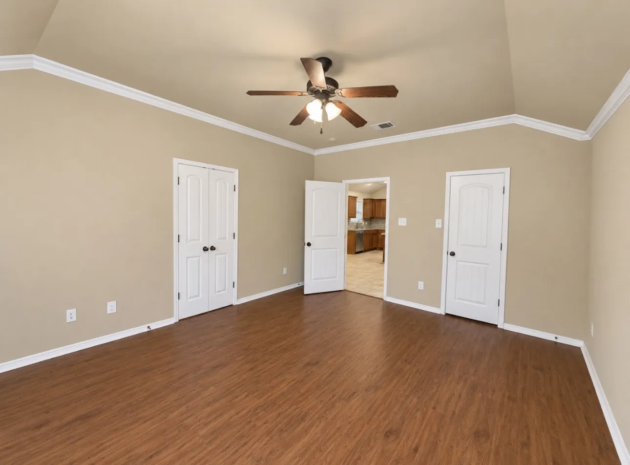 Vaulted ceiling with crown molding, wood-finish flooring, and a ceiling fan