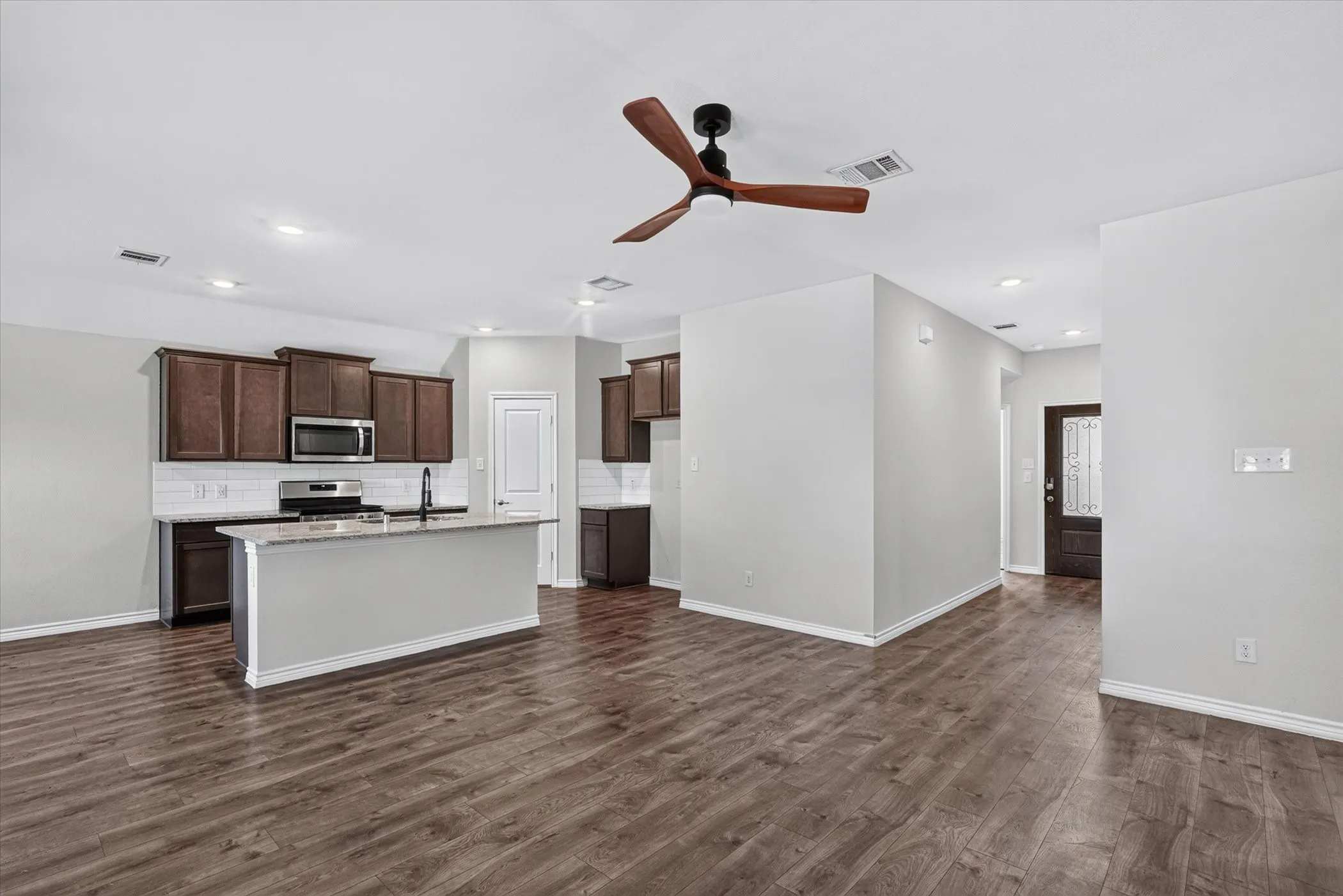 Spacious open-concept living area with wood-finish flooring, recessed lighting, and a modern ceiling fan