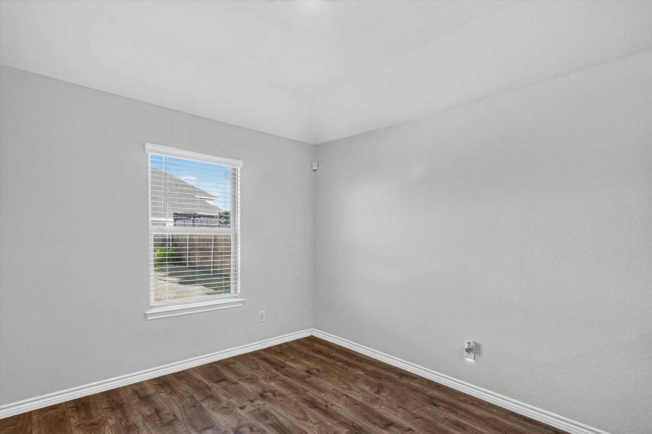 Neutral tone wall finish with wood-finish flooring, white window frame, and white trim