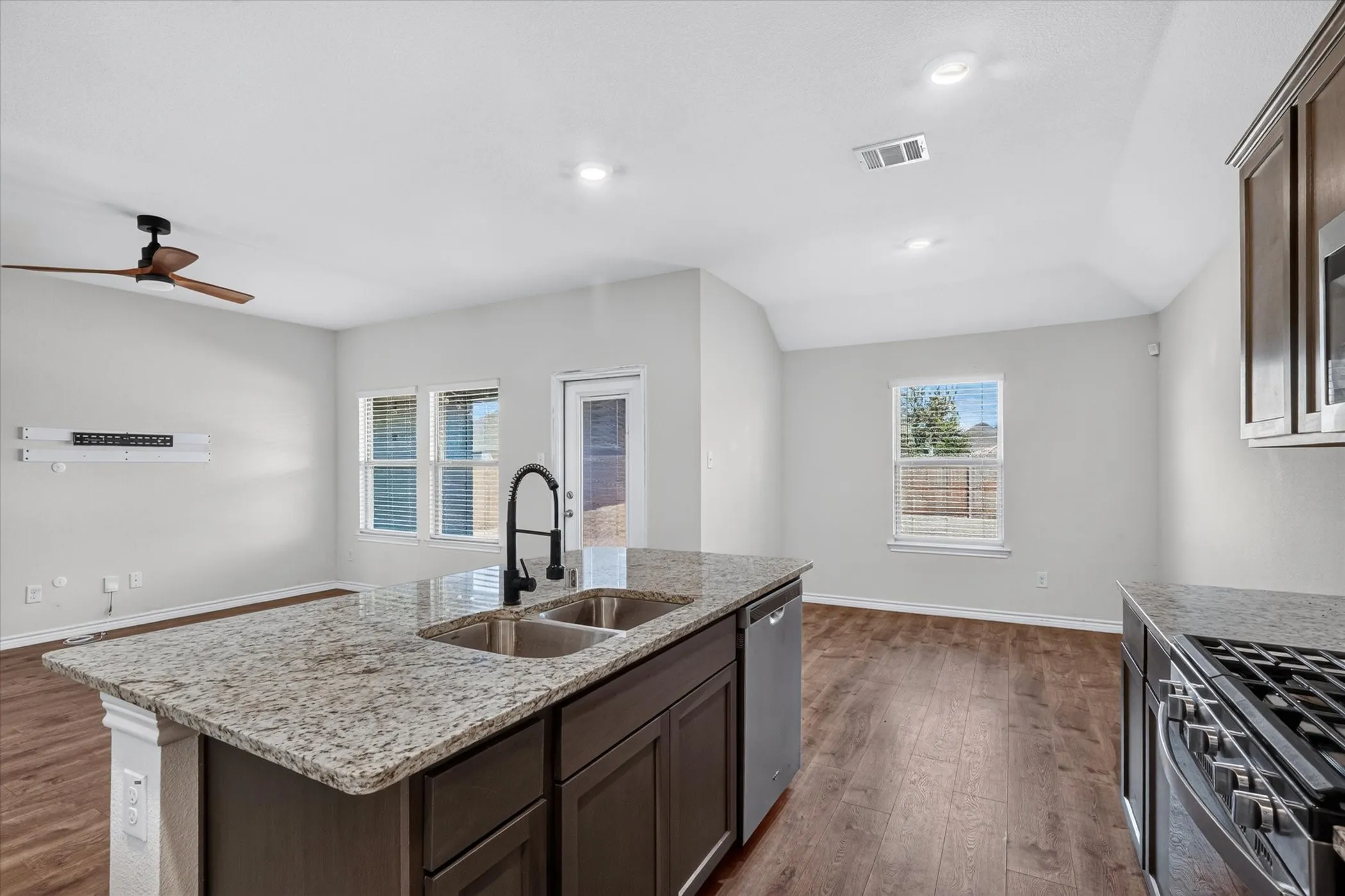 Kitchen island with granite countertop, stainless steel double sink, and dark wood cabinetry