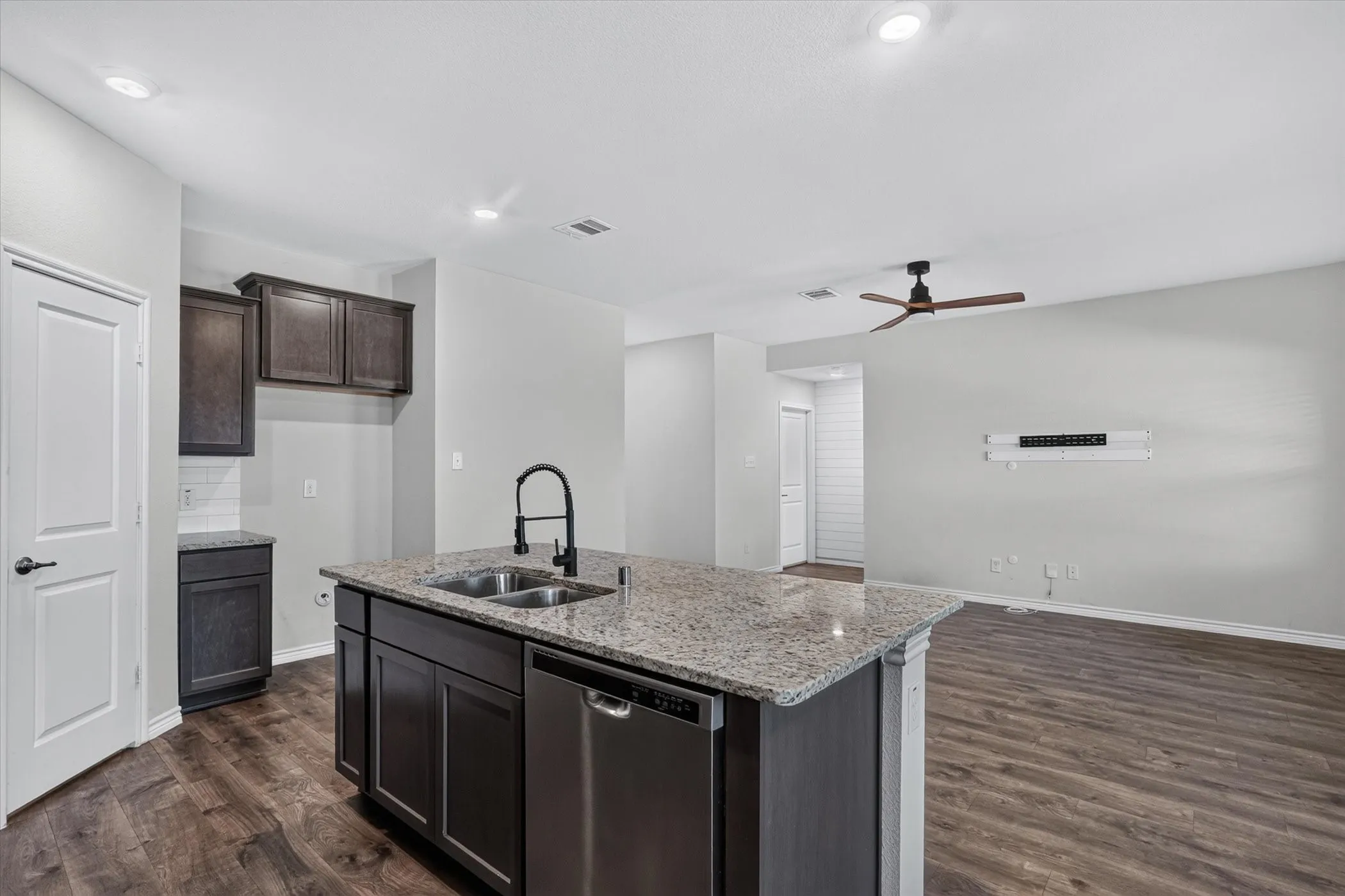 Kitchen island with granite countertops and a stainless steel sink, wood-finish flooring, recessed lighting, ceiling fan, and dark wood cabinetry