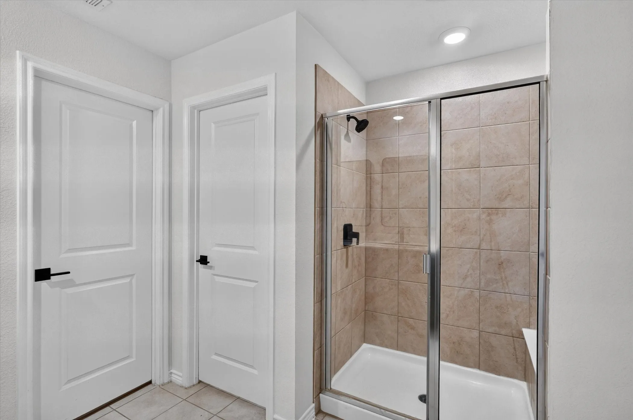 Glass-enclosed shower with tile surround, built-in shelving, and a shower bench