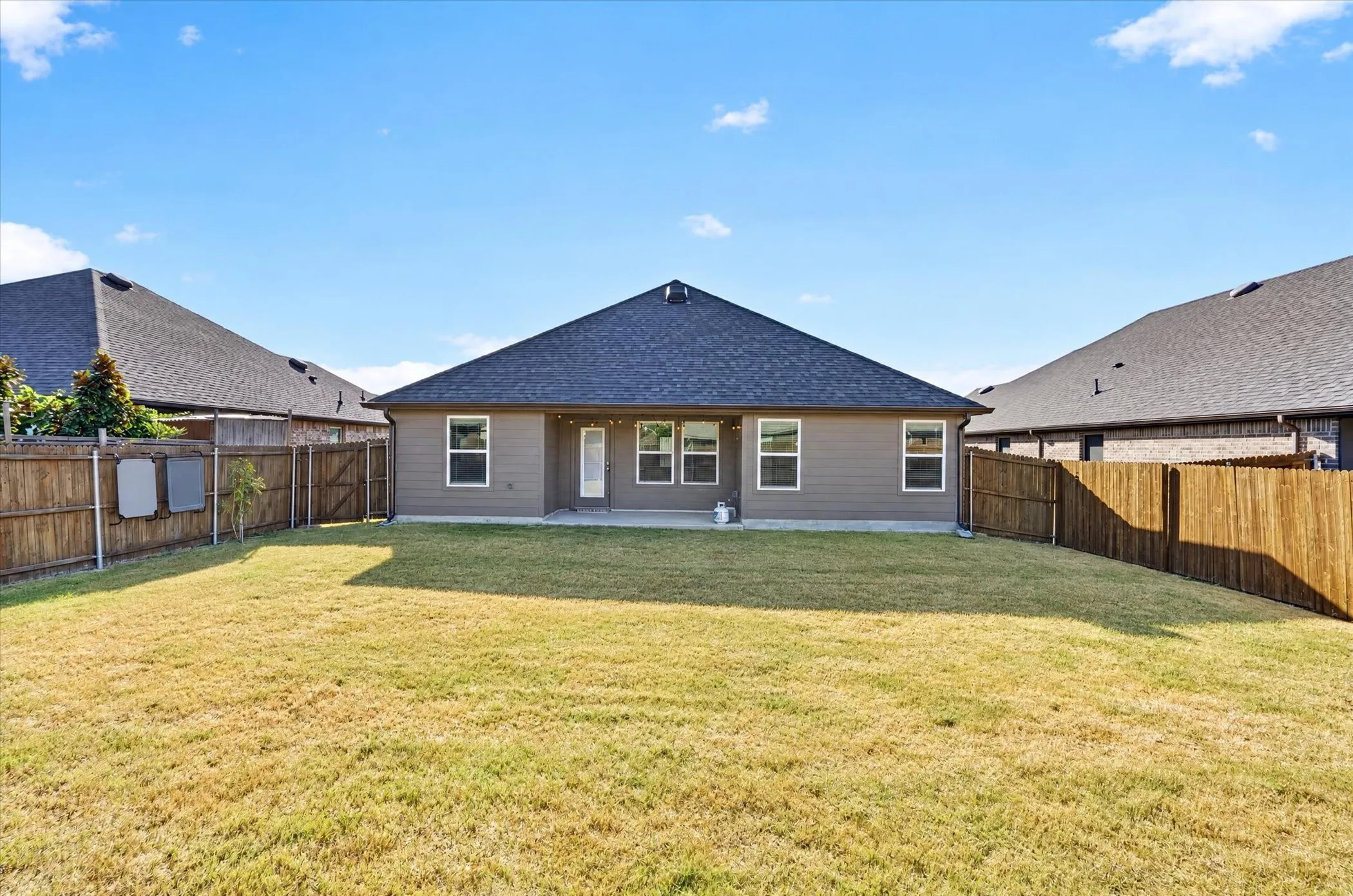 Spacious backyard with a wood privacy fence, concrete patio, and exterior lighting fixtures