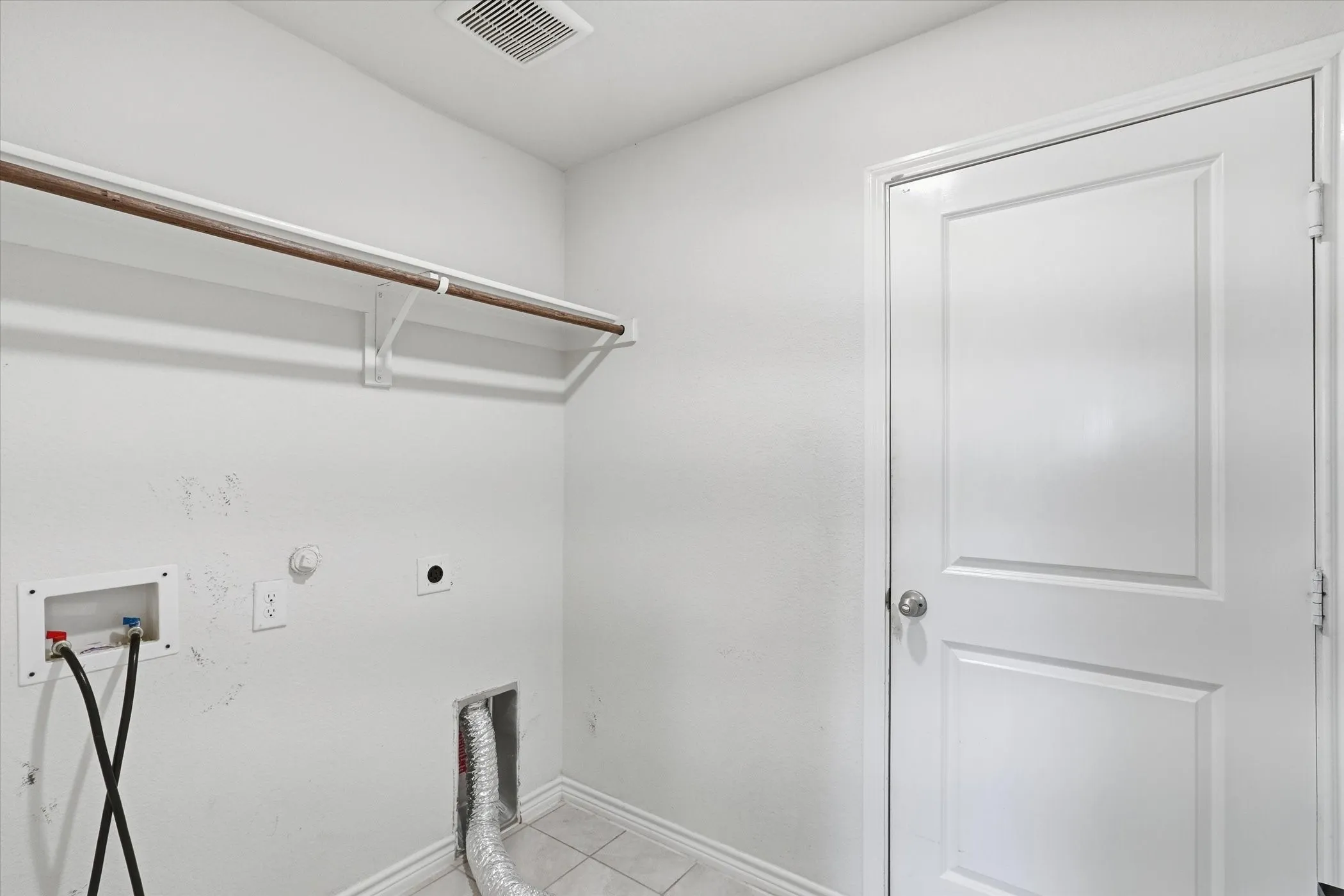 Utility area featuring white walls, tile flooring, and a built-in hanging rod