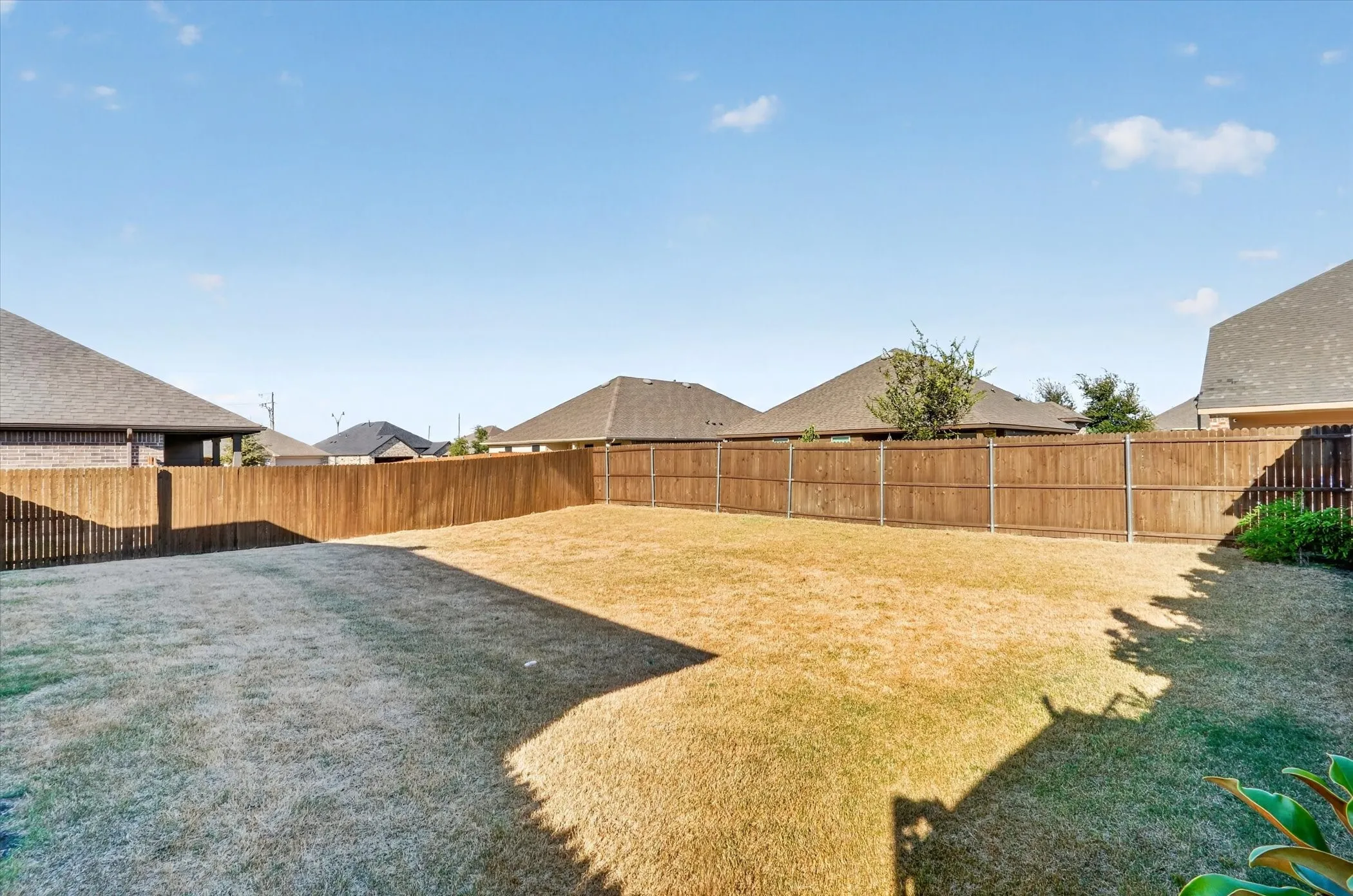 Expansive backyard featuring a generous lawn area, wooden privacy fencing, and mature landscaping