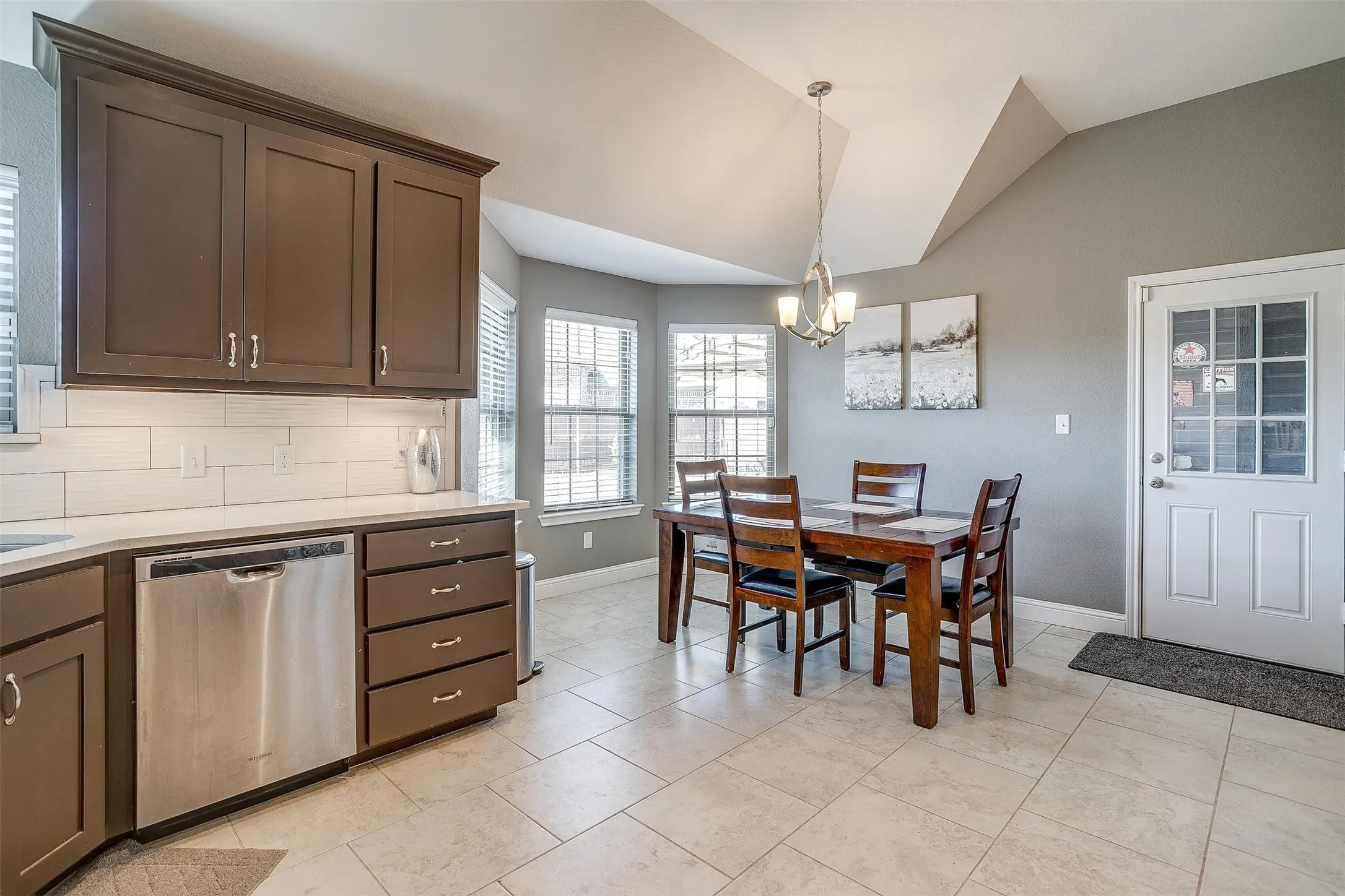 Kitchen with dark wood cabinetry, white subway tile backsplash, light-toned countertop, and stainless steel dishwasher