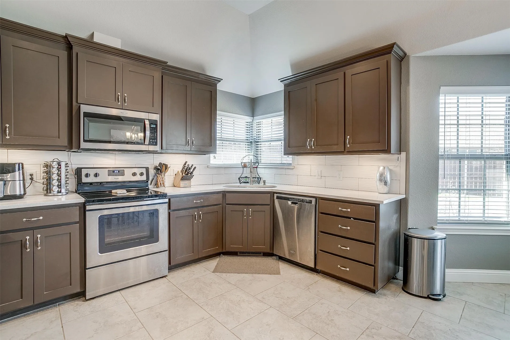 Stainless steel appliances, recessed lighting, white subway tile backsplash, white countertops, and warm-toned cabinetry