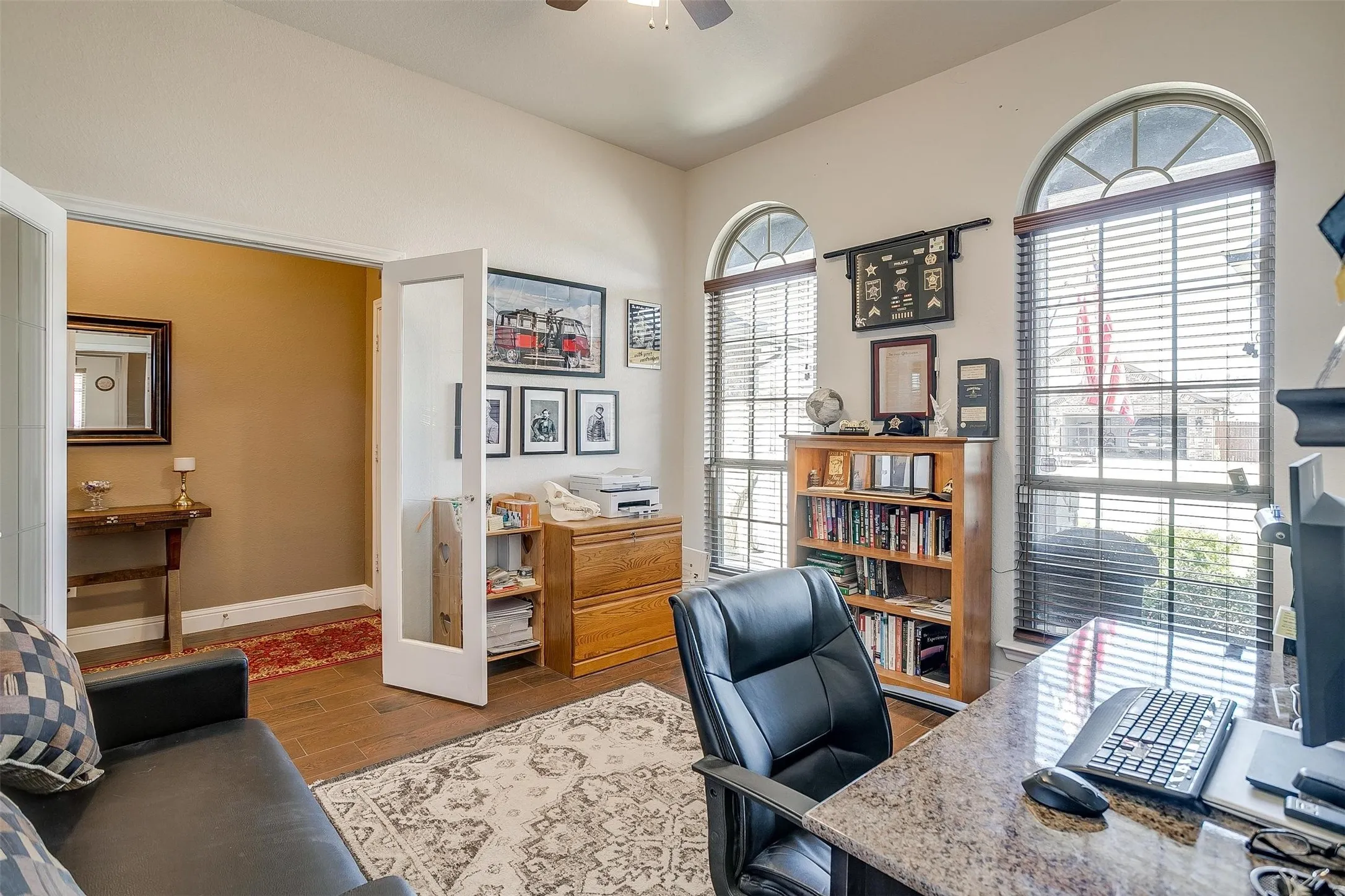 Arched windows, double French doors, wood-finish flooring, and a ceiling fan