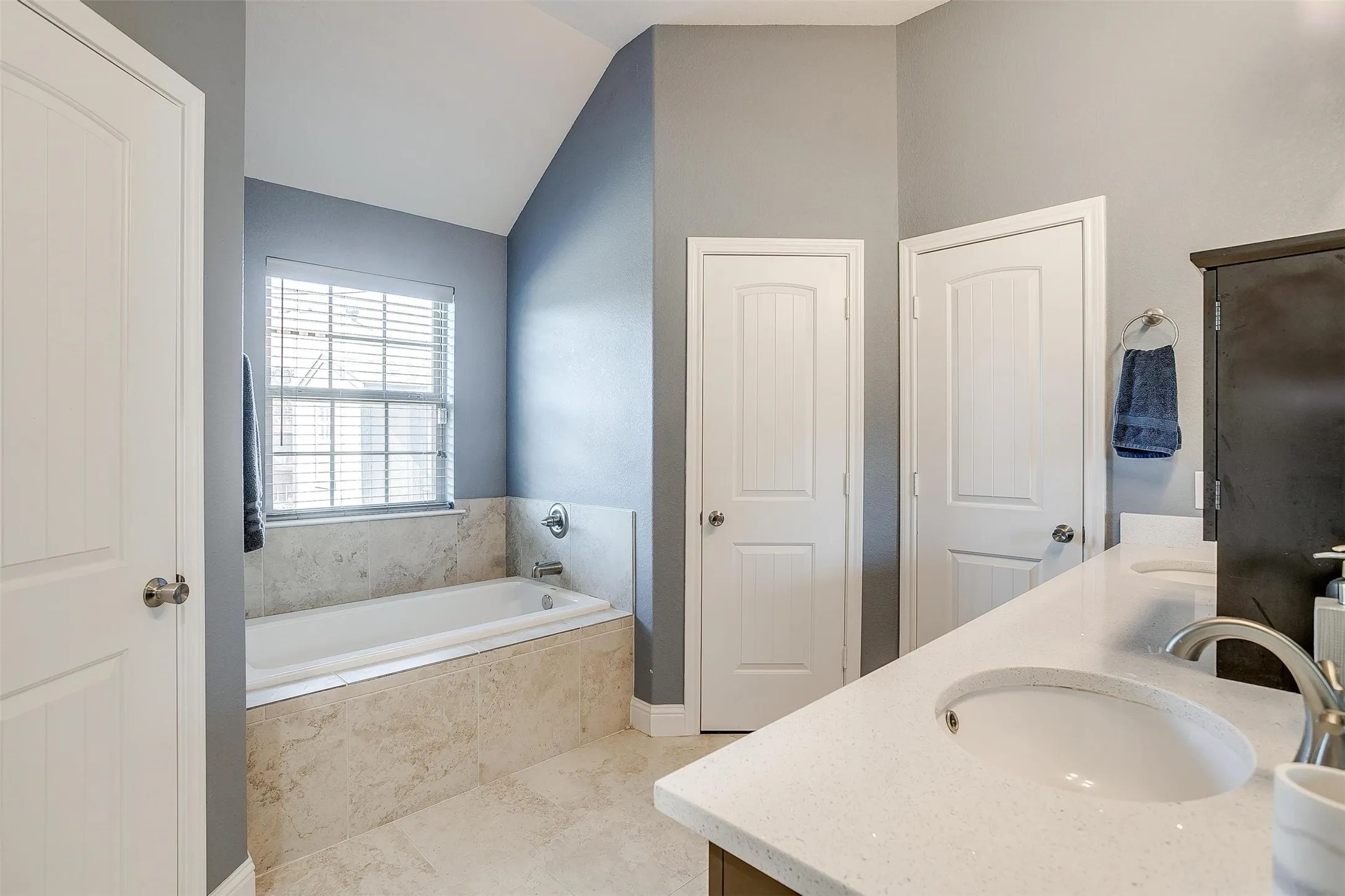 Built-in soaking tub with tile surround, dual vanity with undermount sinks, and light-colored countertops