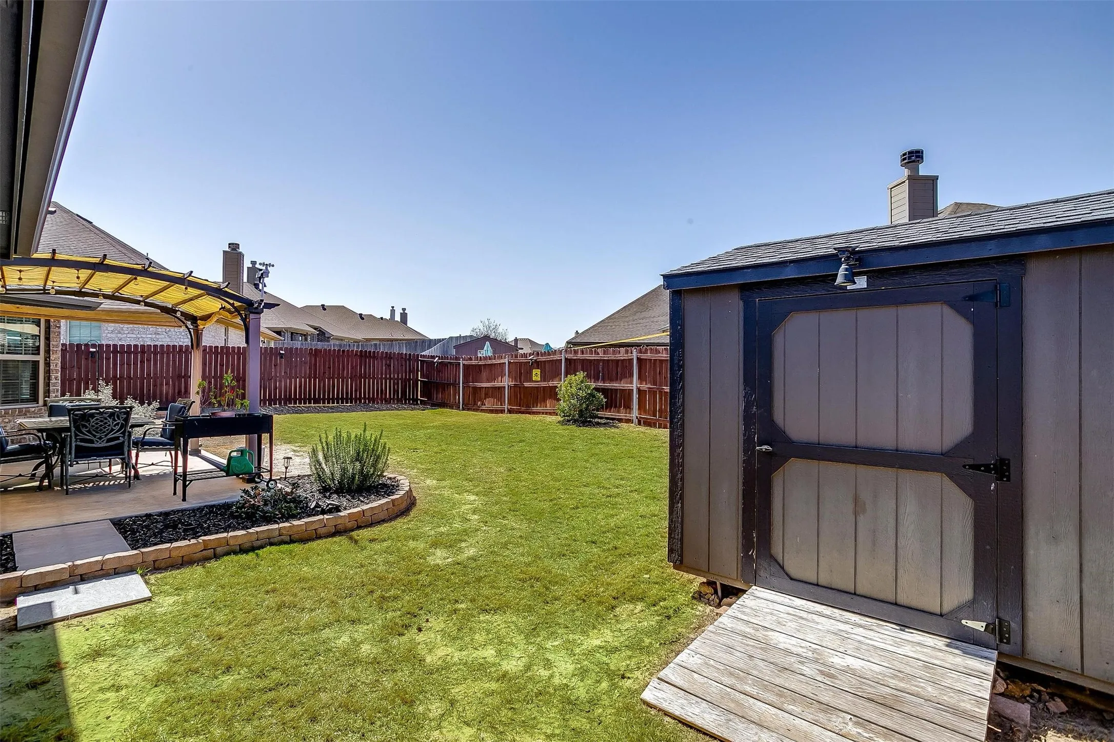 Expansive backyard featuring a lush lawn, privacy fencing, a covered patio area, and a functional storage shed with a ramp