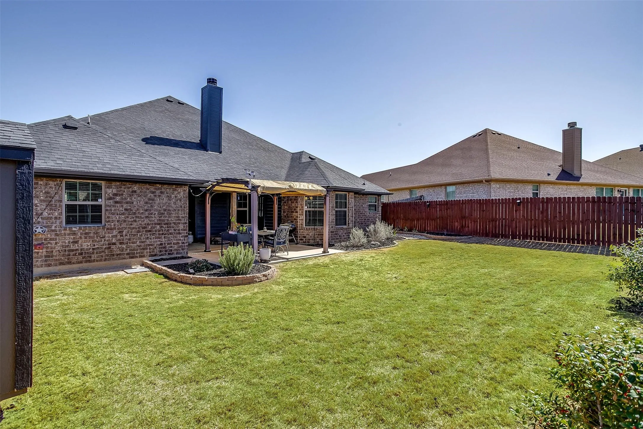 Expansive green lawn with a covered patio area and brick exterior