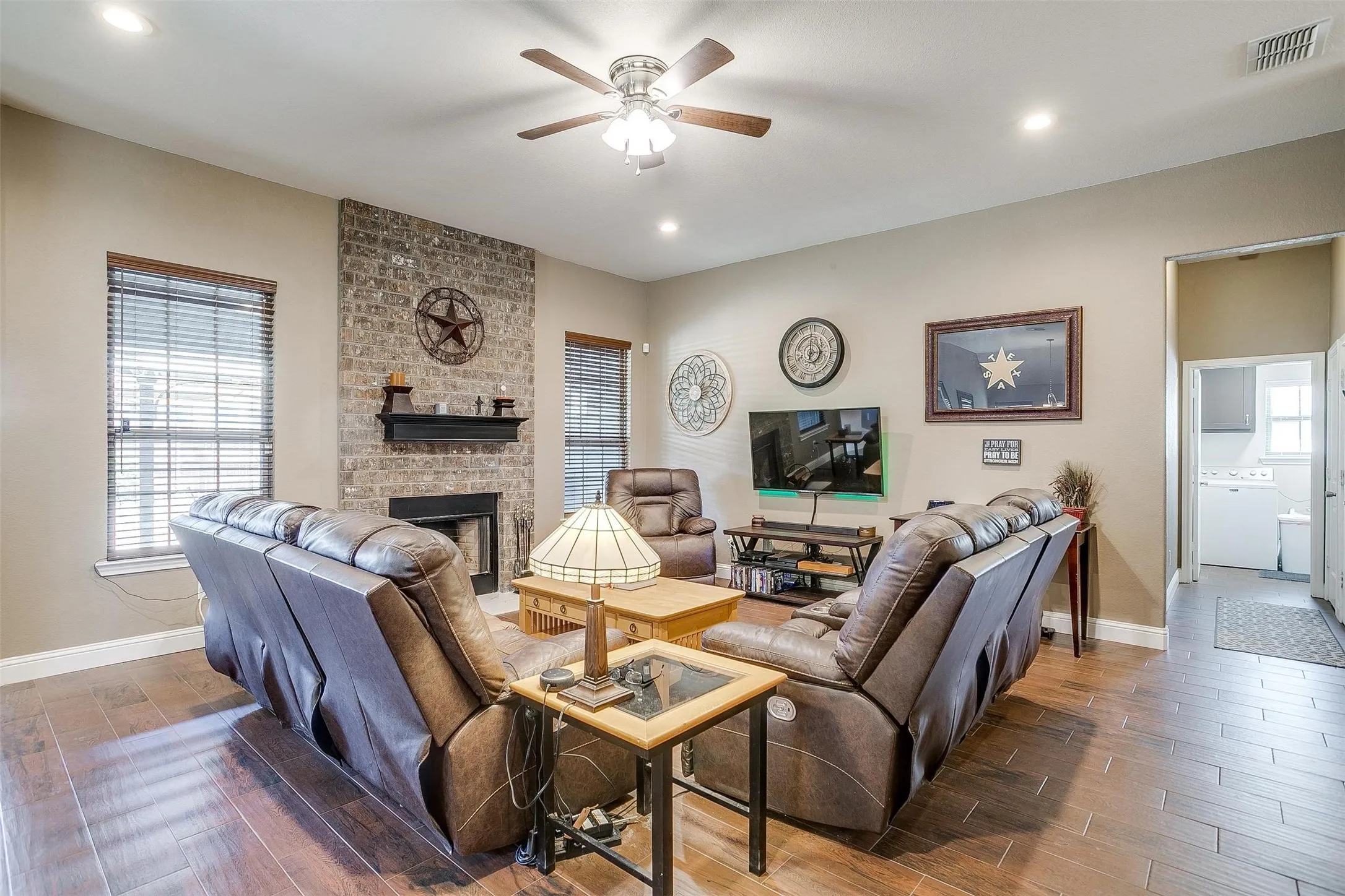 Living area with wood-finish flooring, brick fireplace with mantel, recessed lighting, ceiling fan, and window blinds