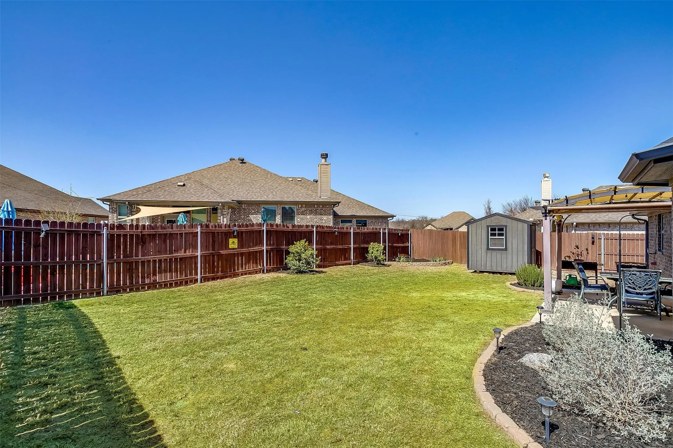 Expansive lawn area with a perimeter privacy fence, exterior storage shed, and a paved patio area