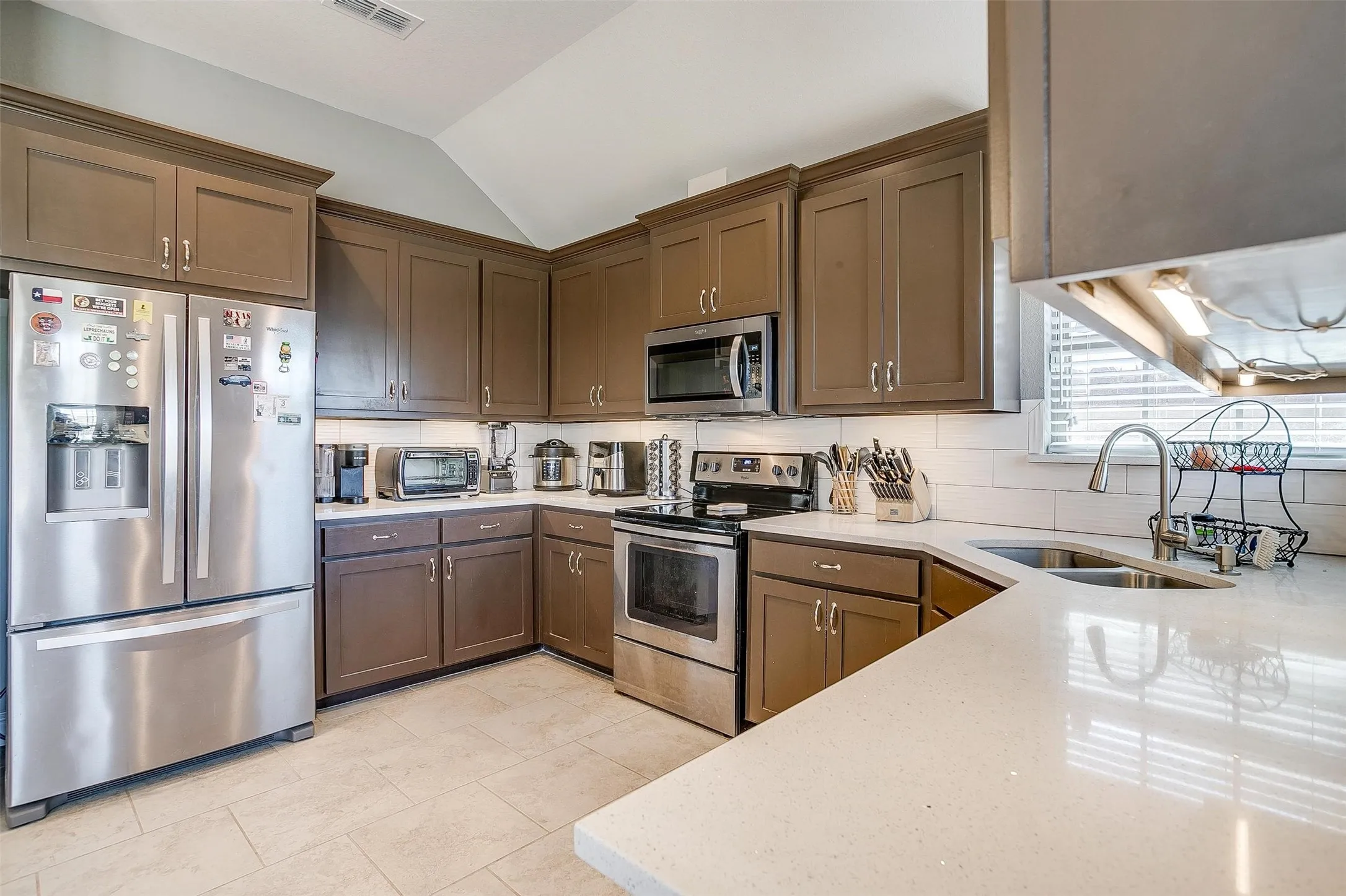 Kitchen featuring stainless steel appliances, extensive cabinetry, light-toned countertops, and a white subway tile backsplash