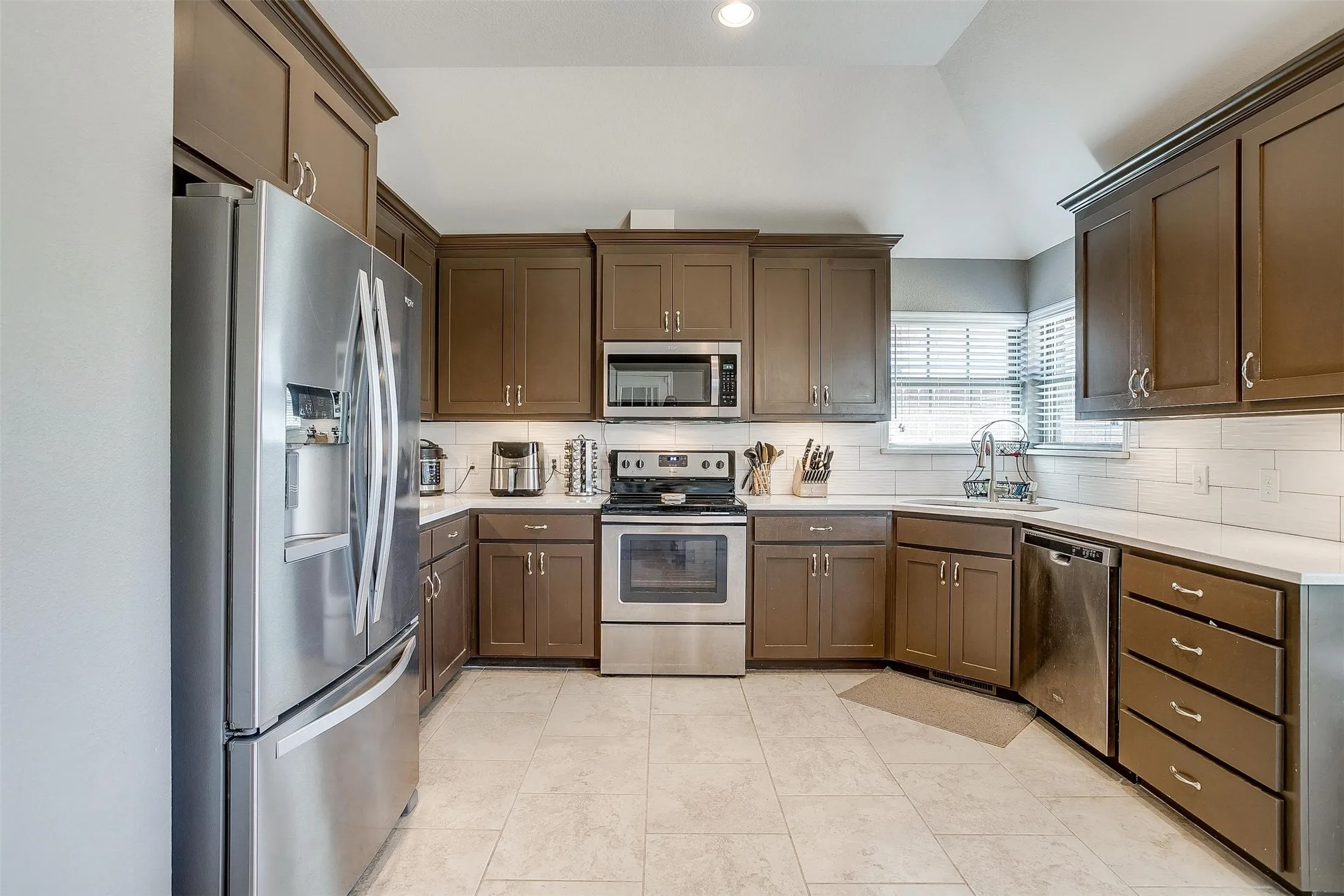 Kitchen featuring extensive cabinetry, stainless steel appliances, white subway tile backsplash, light-toned countertops, and tile flooring