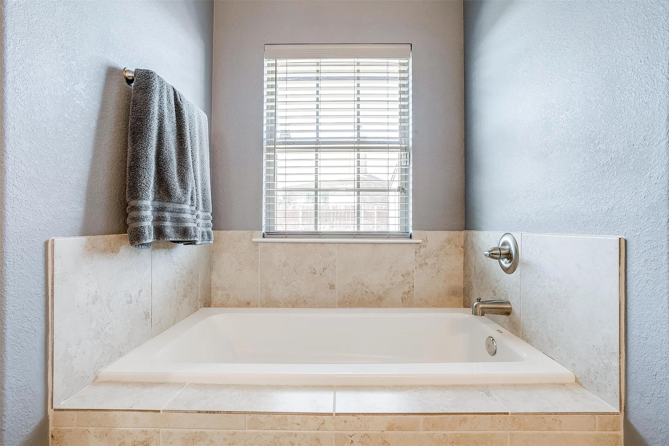 Built-in soaking tub with a tiled surround, brushed nickel fixtures, and privacy blinds