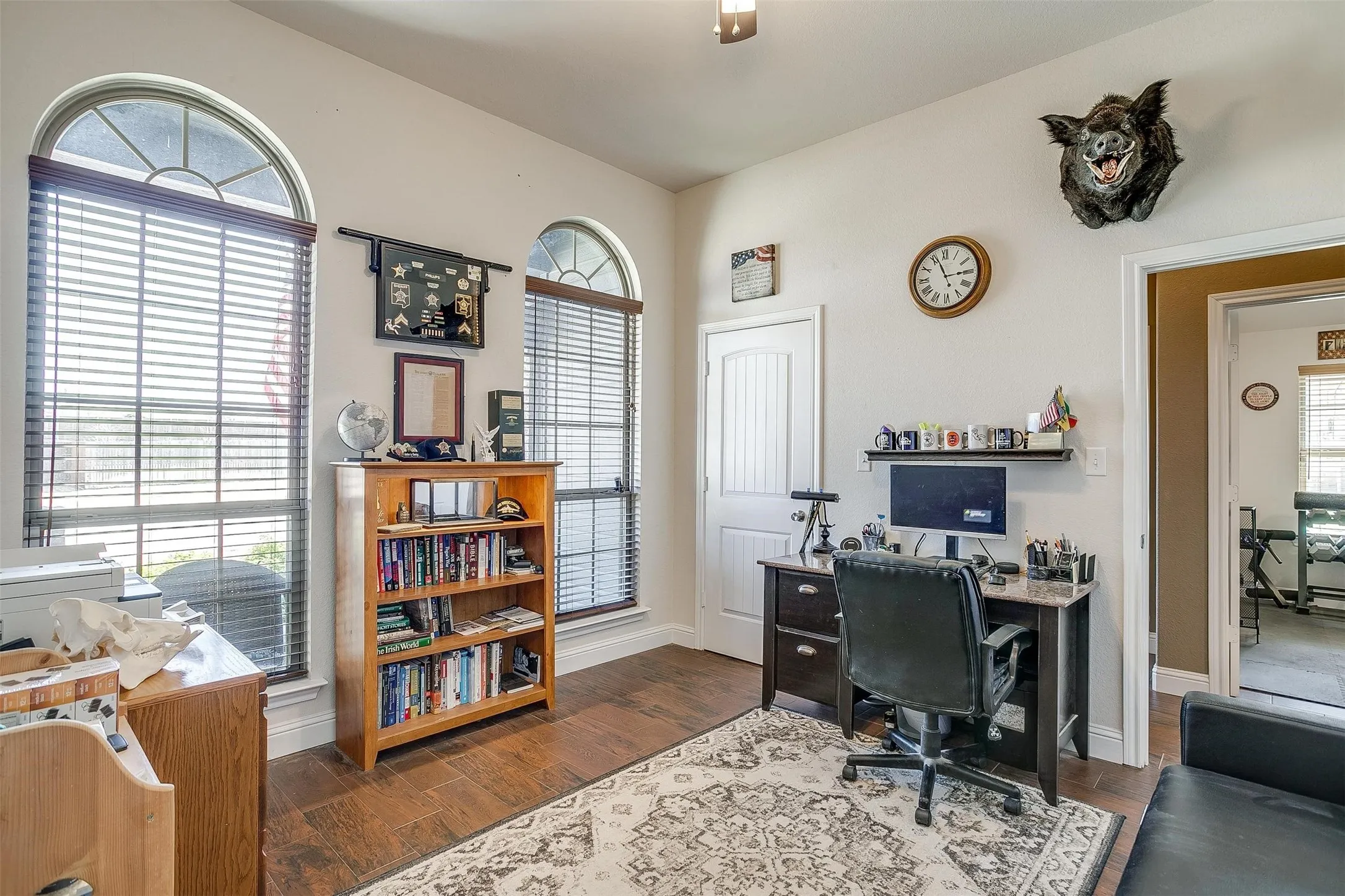 Wood-finish flooring, two arched windows with blinds, a built-in shelf, and a white paneled door