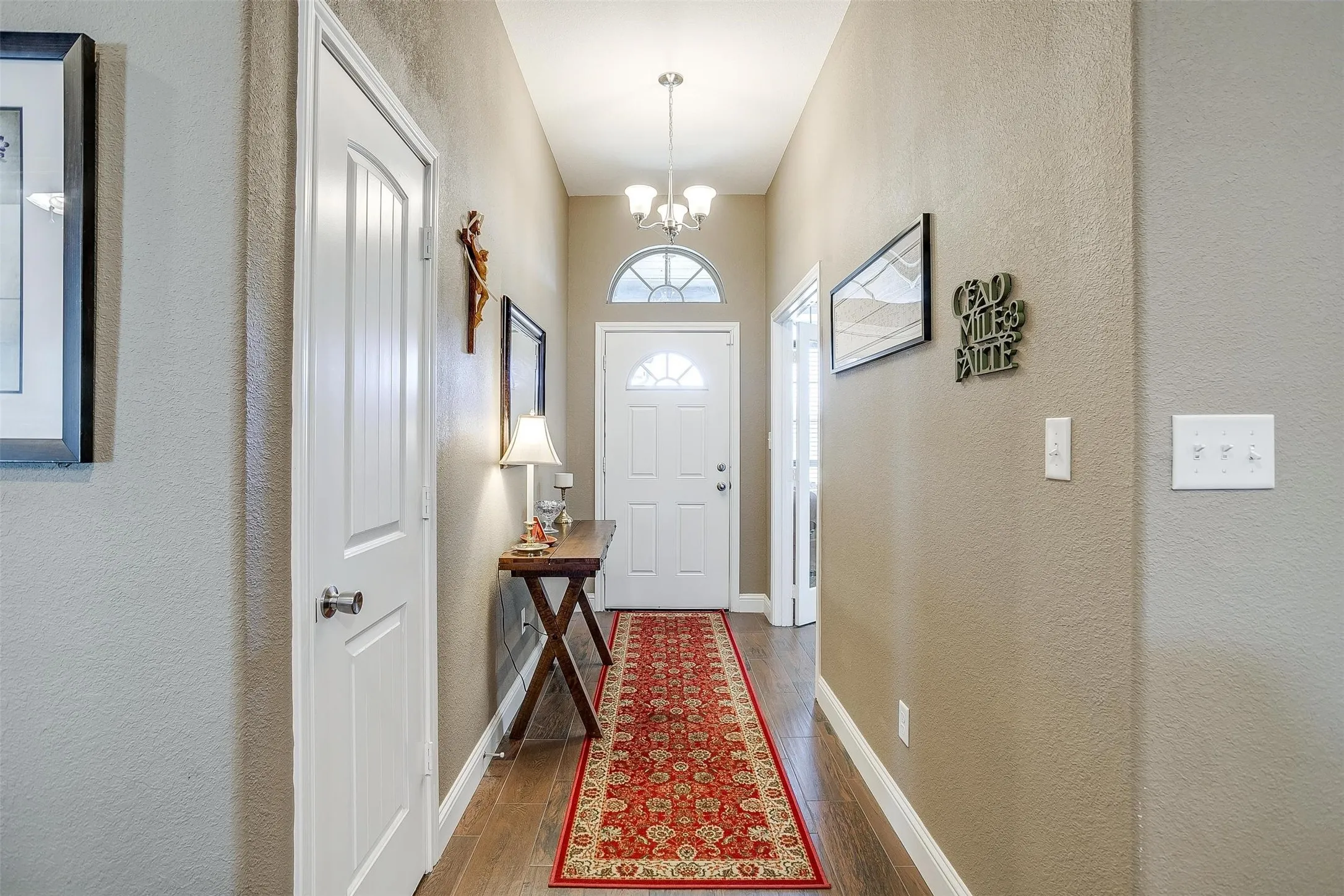 Arched transom window above the entry door, wood-finish flooring, and a ceiling-mounted chandelier