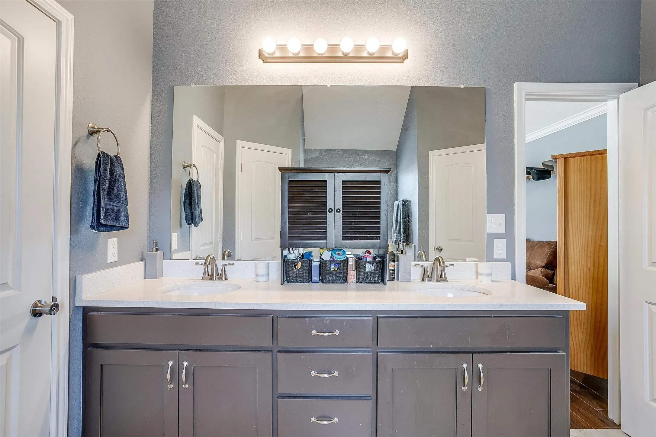 Dual basin vanity with a light-toned countertop, gray cabinetry, and an expansive mirror