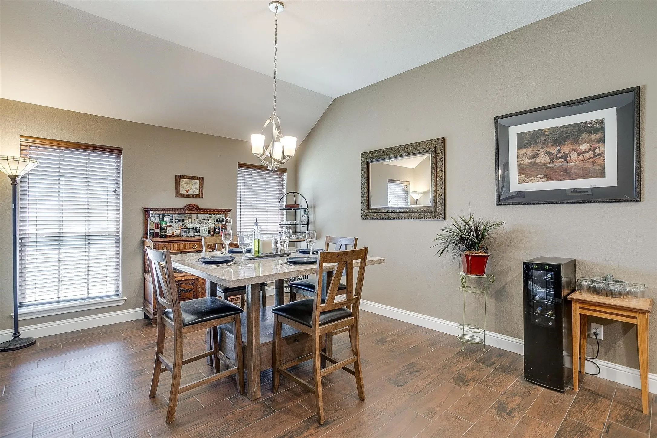 Vaulted ceiling with a chandelier, wood-finish flooring, and two windows with blinds