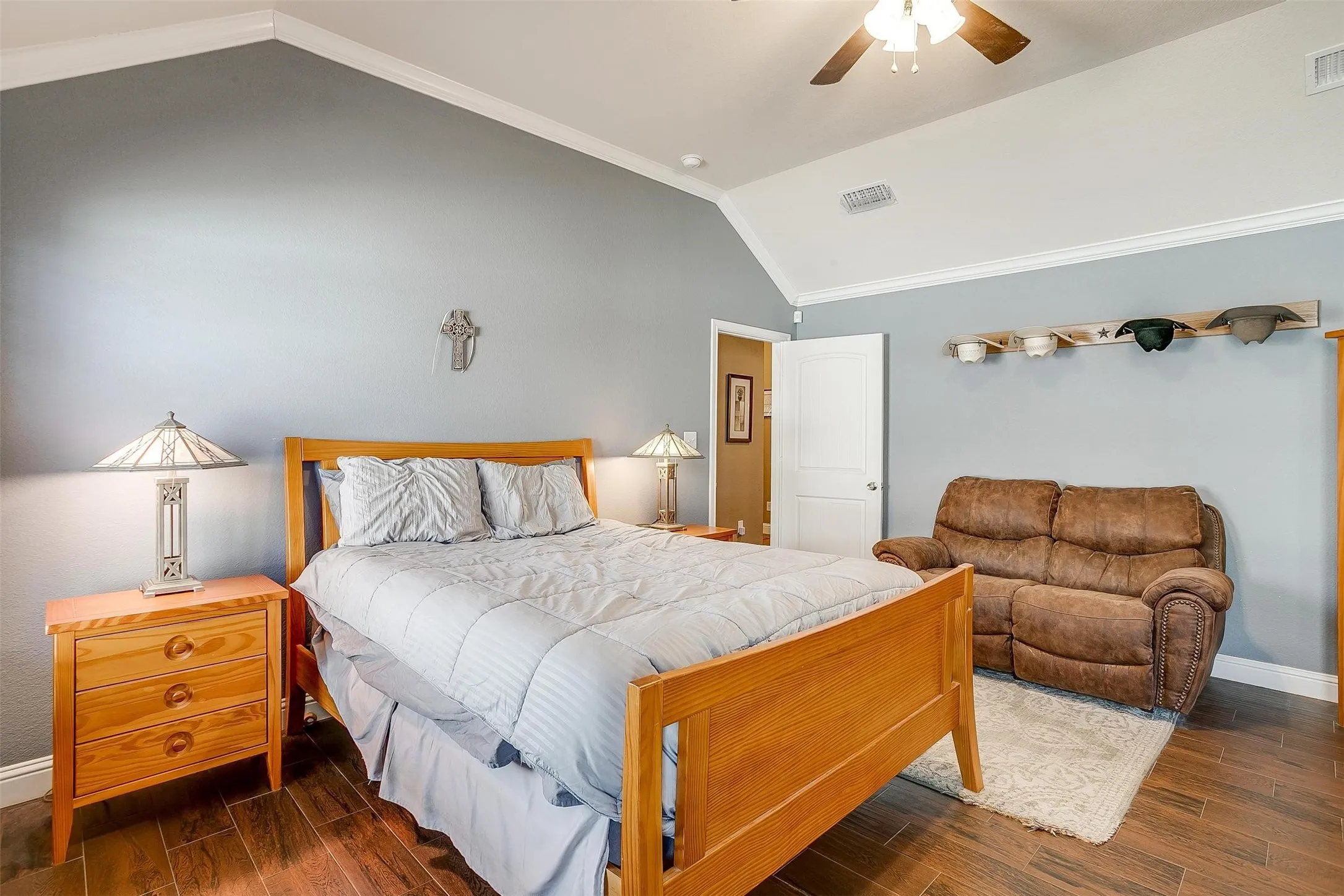 Vaulted ceiling with crown molding, wood-finish flooring, ceiling fan with integrated lighting, and a white paneled door