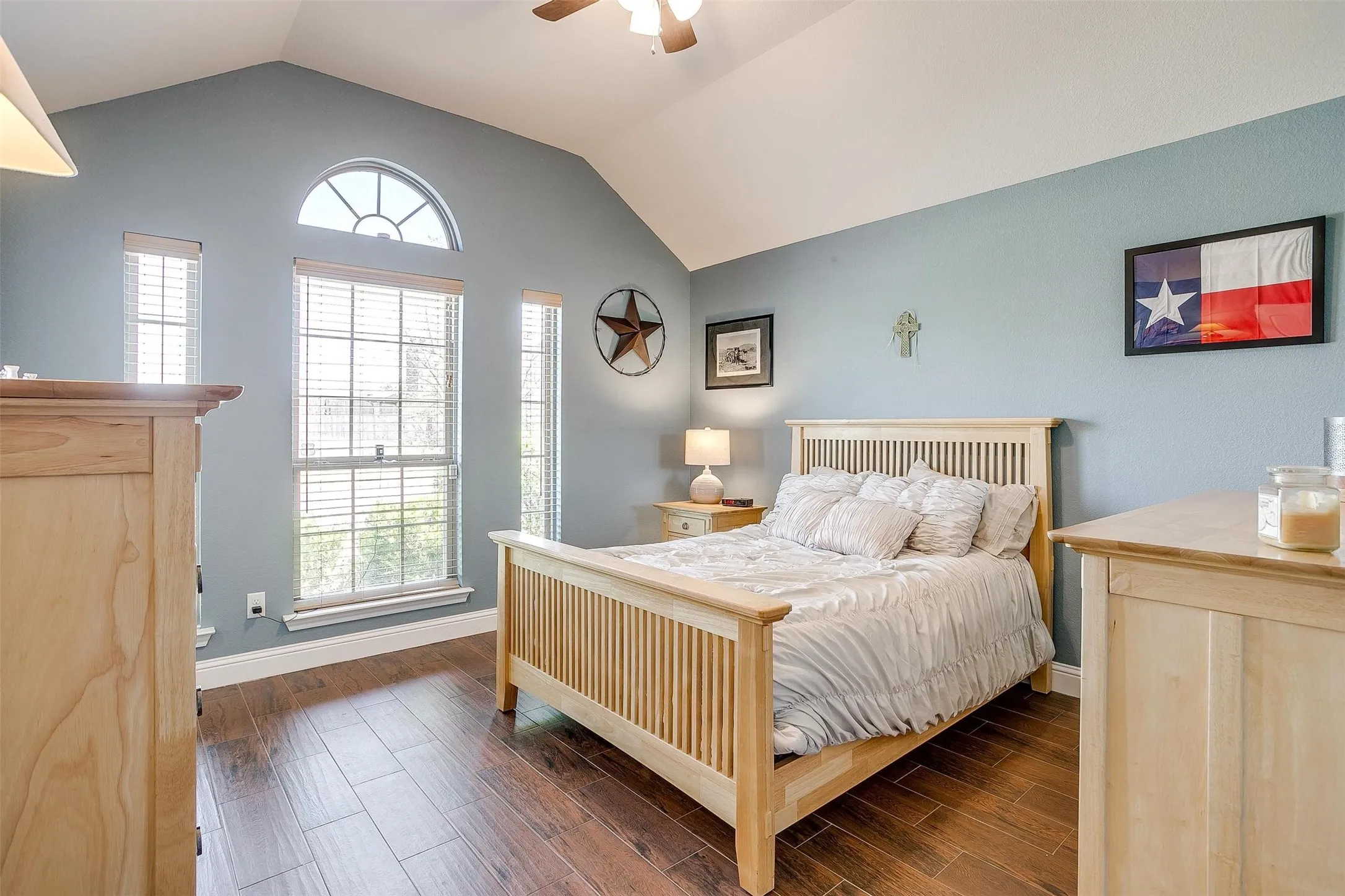 Vaulted ceiling, arched transom window, wood-finish flooring, ceiling fan, and multiple windows