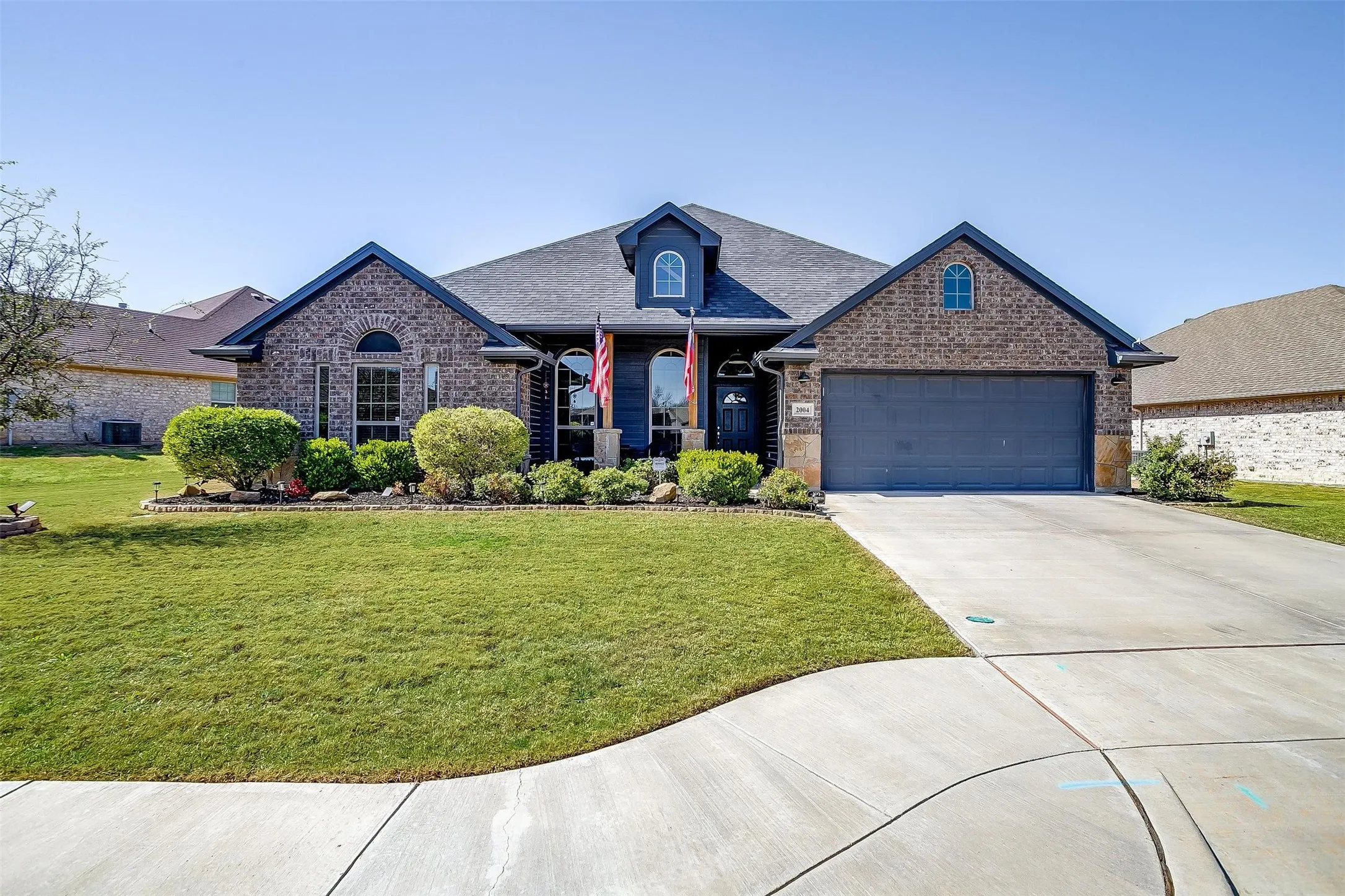 Brick exterior with dark trim accents, concrete driveway, attached garage, and landscaped front yard