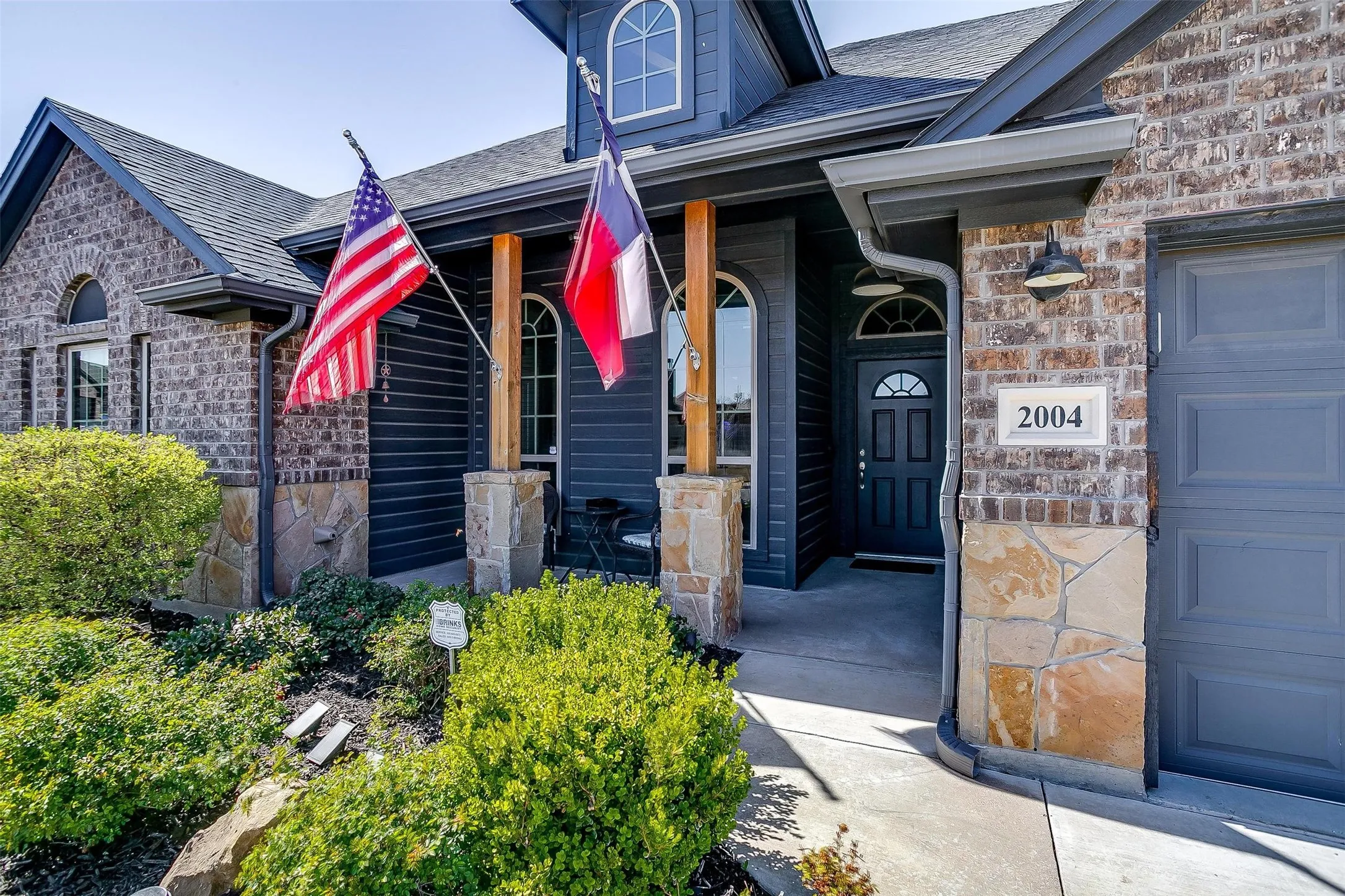 Brick and stone facade with wood accents, featuring a dark gray garage door, covered entry, and mature landscaping