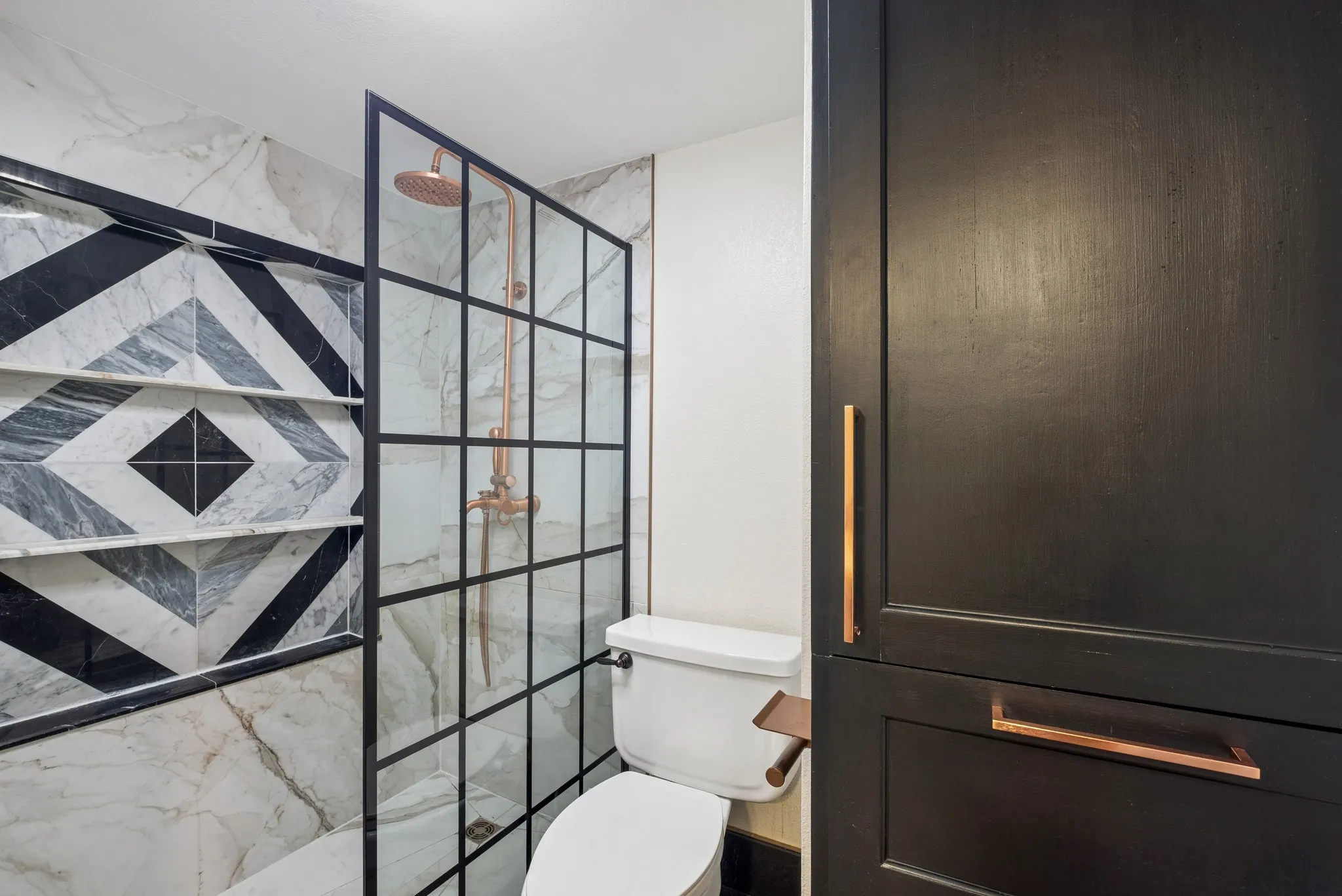 Walk-in shower with a grid-pattern glass enclosure, rainfall showerhead, built-in shelving, and black wood-finish cabinetry with copper-tone hardware