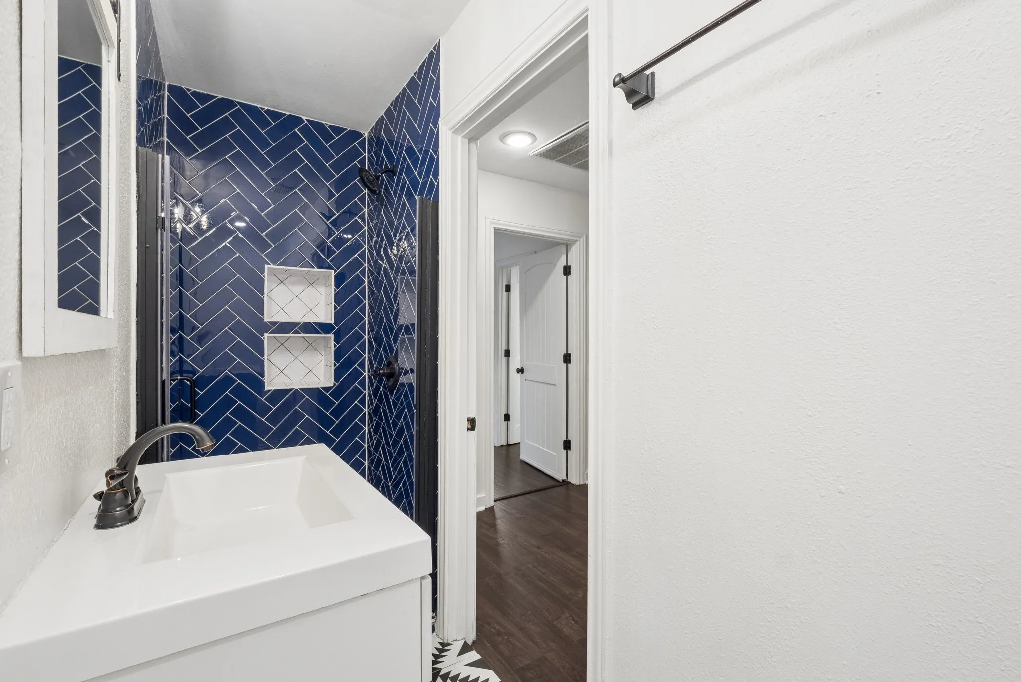 Bathroom featuring a vanity with an integrated sink, dark bronze-finish faucet, and a tiled shower with a herringbone pattern and recessed shelving