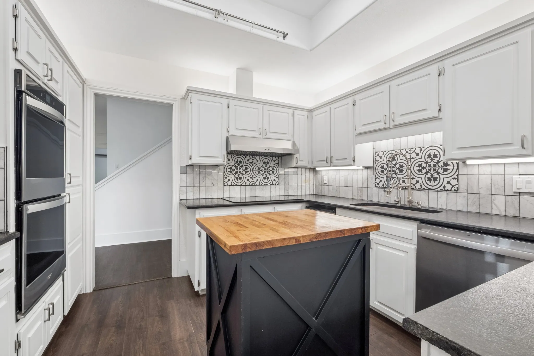 Kitchen featuring light gray cabinetry, dark countertops, black and white tile backsplash, stainless steel appliances, and a central island with a wood-finish top