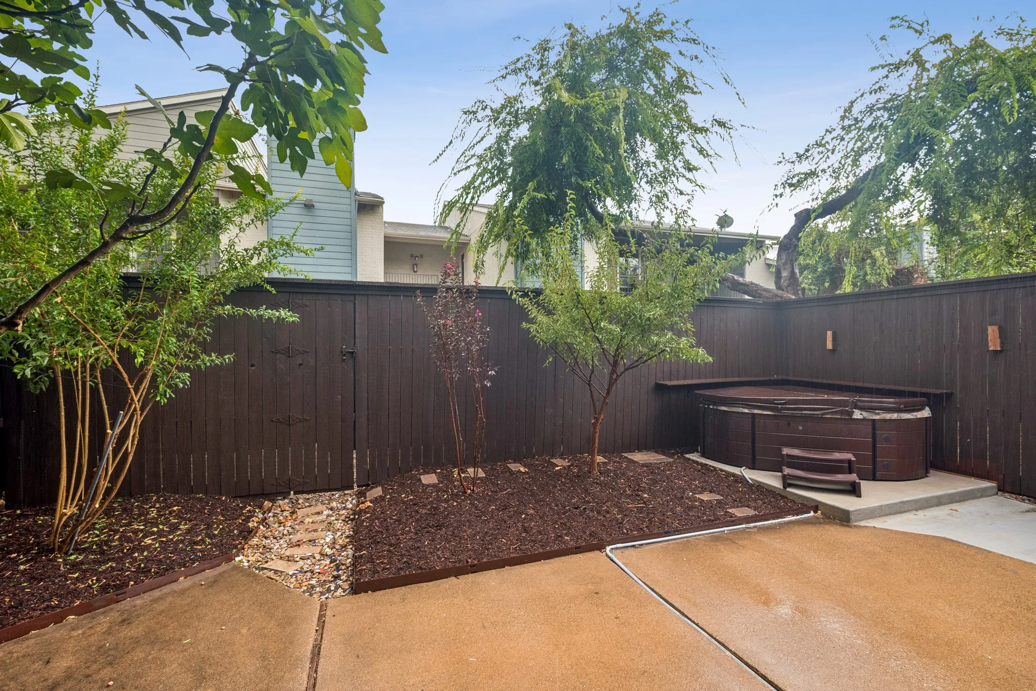 Private fenced patio featuring a built-in spa with steps, concrete patio surface, and landscaped planting beds