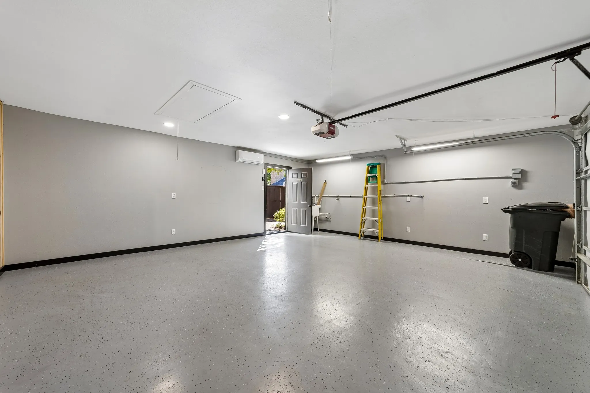 Spacious garage with light grey epoxy flooring, overhead track lighting, and a mini-split air conditioning unit