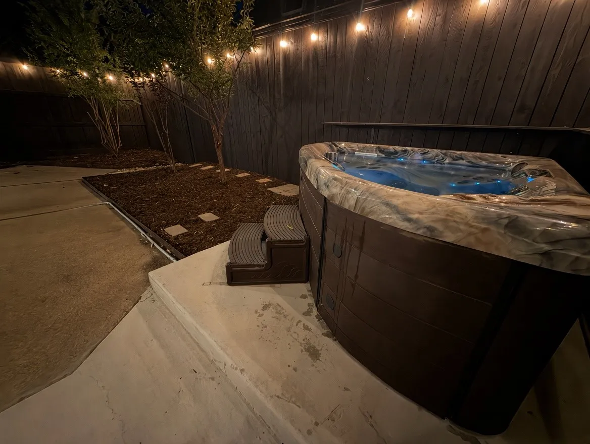 Outdoor space featuring an inset spa, concrete patio, privacy fencing, and mature trees