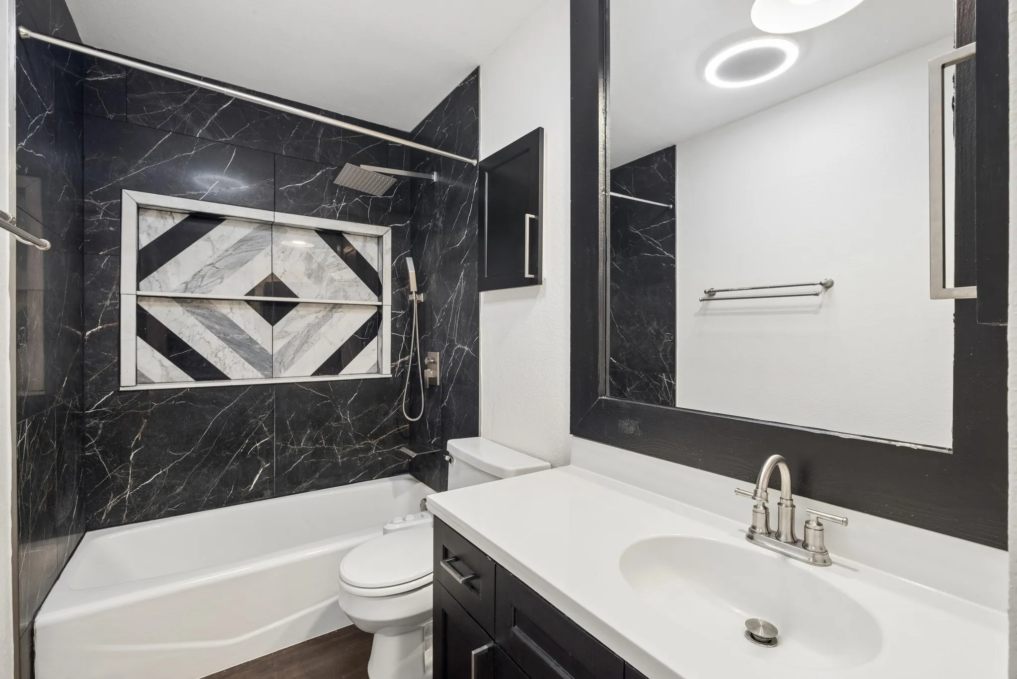 Bathtub with black-veined wall tile, decorative shower niche, and rainfall showerhead