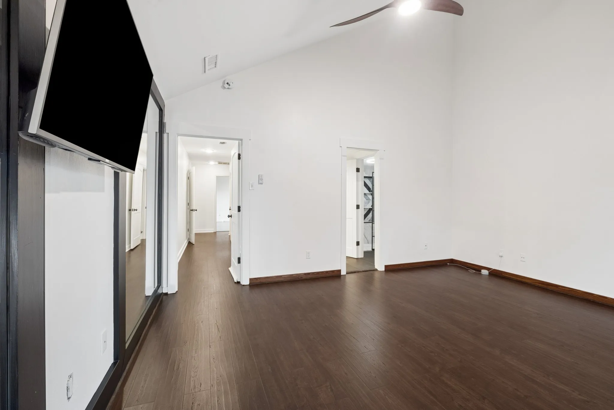 Vaulted ceiling with a ceiling fan, dark wood-finish flooring, and white walls
