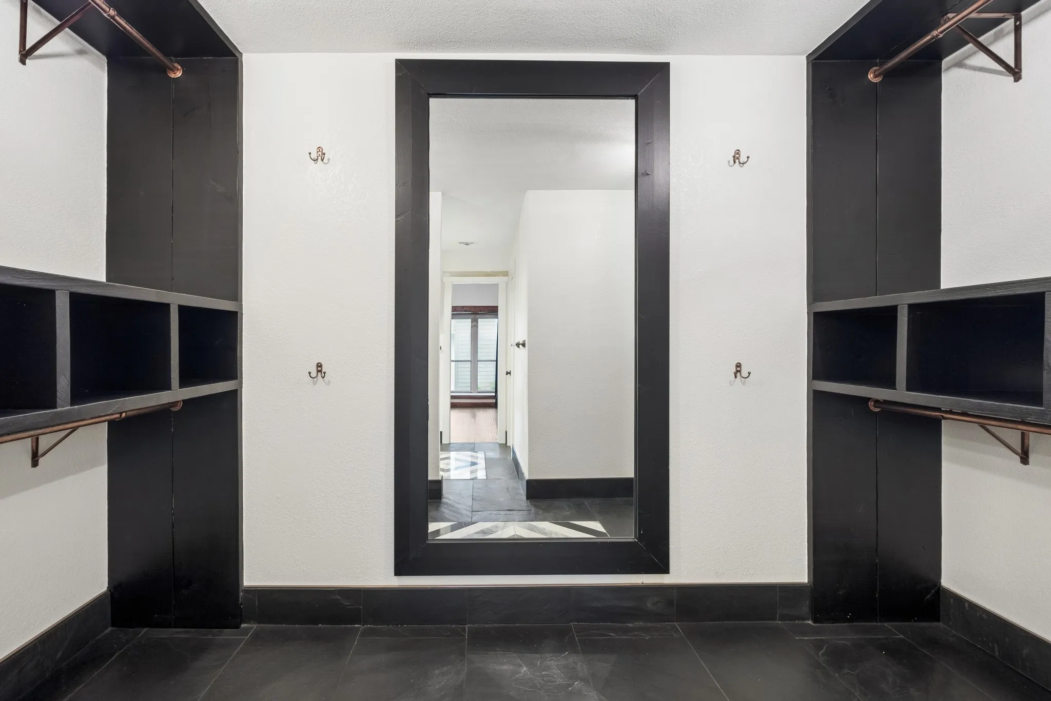 Integrated shelving units with copper-toned hanging rods, built-in mirror, and dark tile flooring