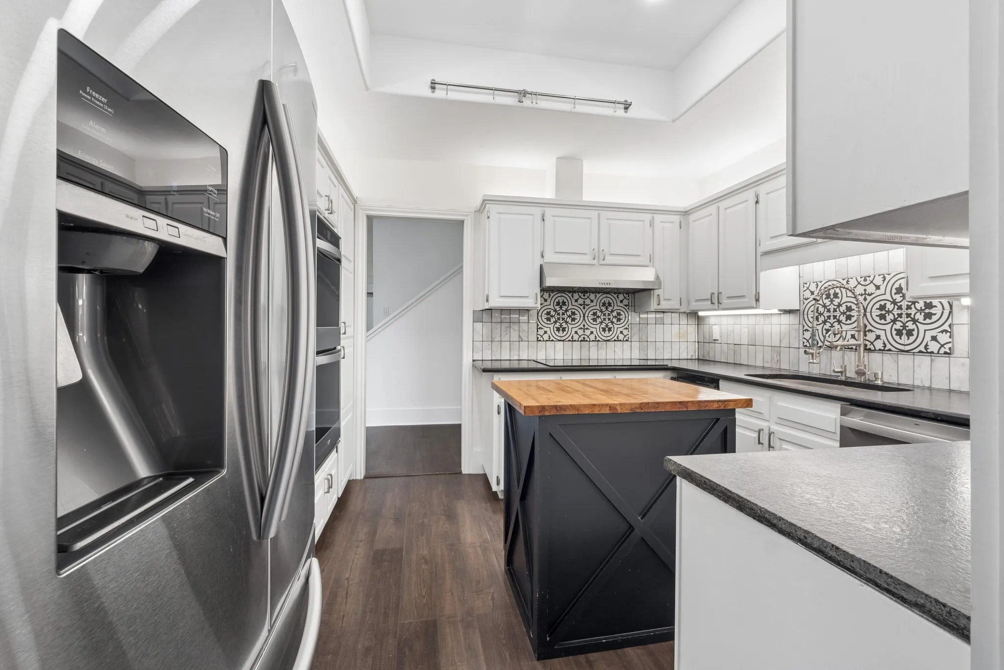 Stainless steel refrigerator, wood-finish flooring, light-toned cabinetry, patterned tile backsplash, and a central island with a wood-finish countertop