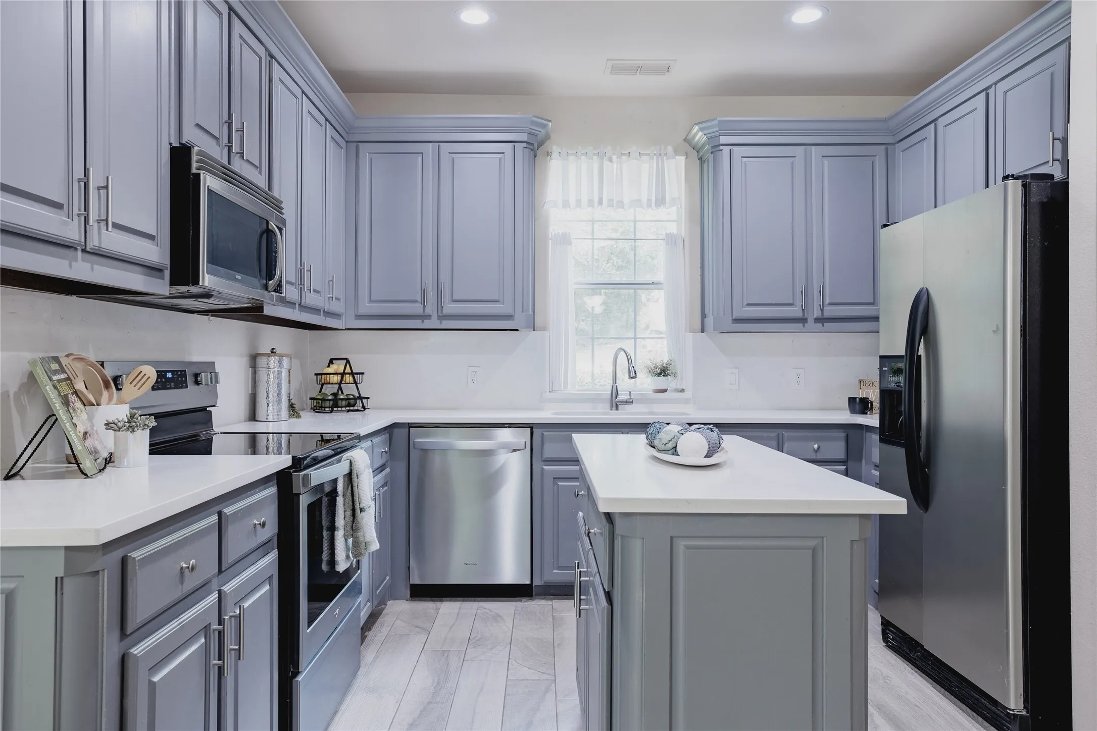 Gray shaker cabinetry, stainless steel appliances, white countertops, center island, and light wood-finish flooring