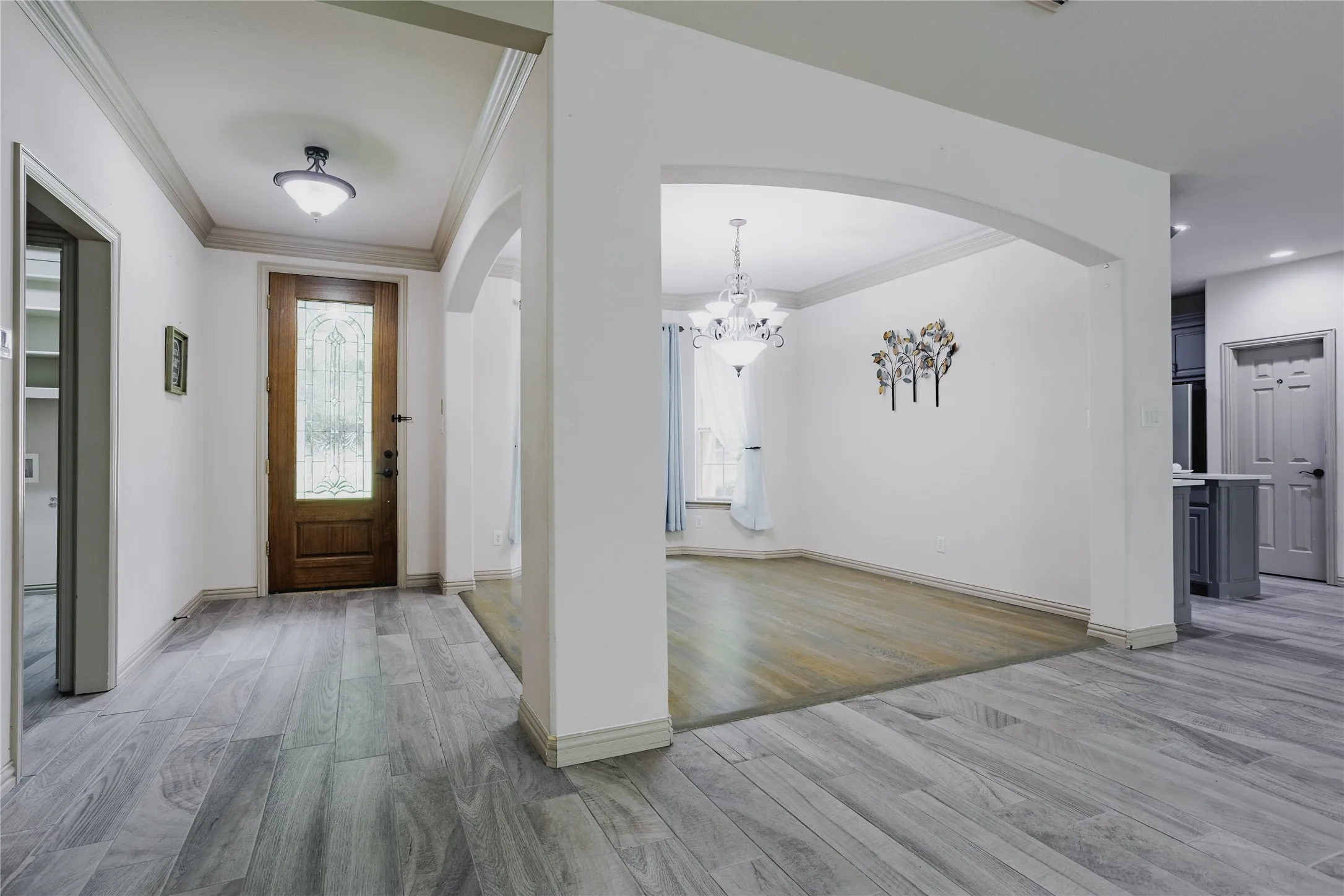 Wood-finish flooring throughout, arched doorways, a wood-paneled entry door with leaded glass, and crown molding