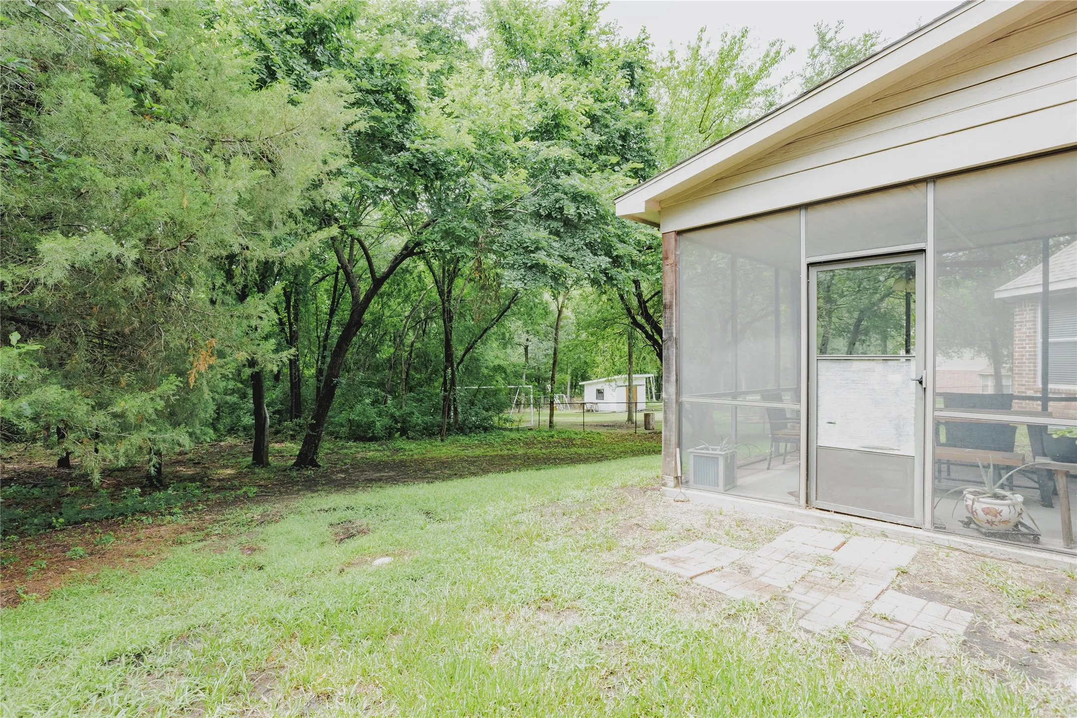 Screened-in porch featuring a glass-paneled door, brick patio pavers, and mature trees in the surrounding landscape
