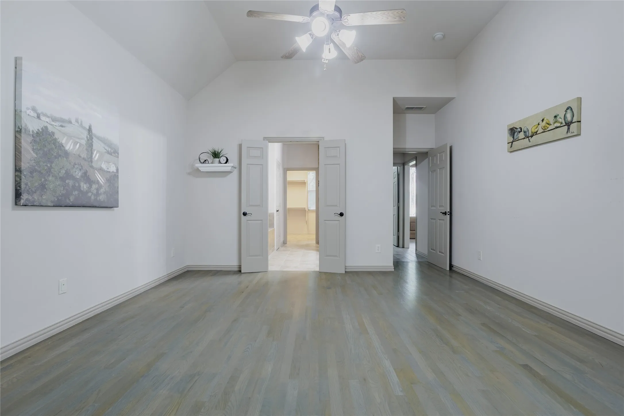 Vaulted ceiling with a ceiling fan, wood-finish flooring, and white interior doors
